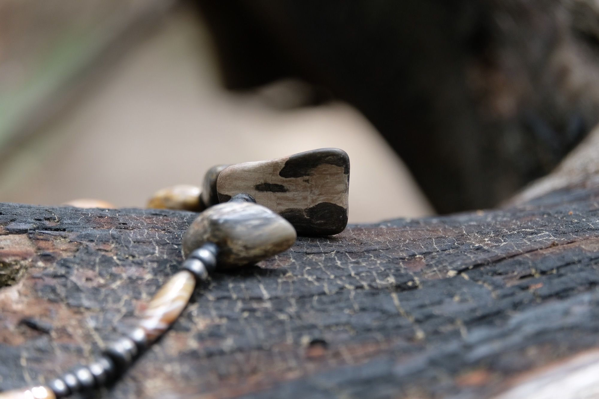 Detail of necklace with petrified wood and black beads sitting on a burned log