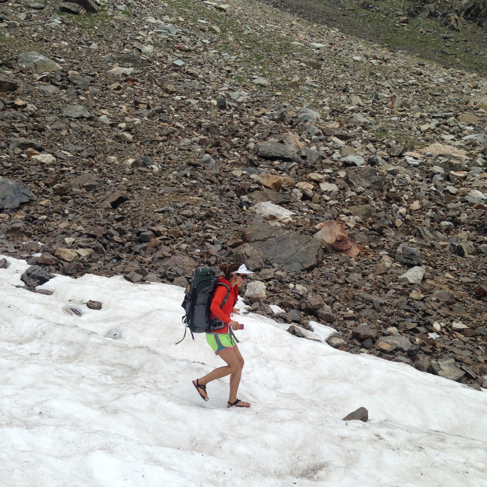 Woman wearing orange shirt and large backpack walks on a snow covered spree field