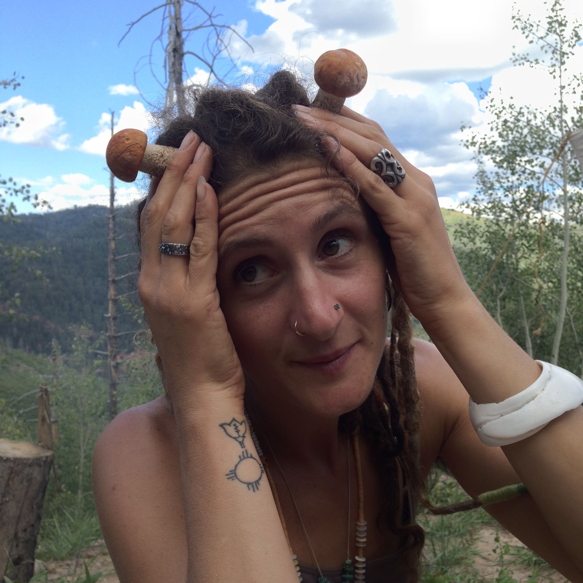 A woman holds two small mushrooms up to her head like antlers.  