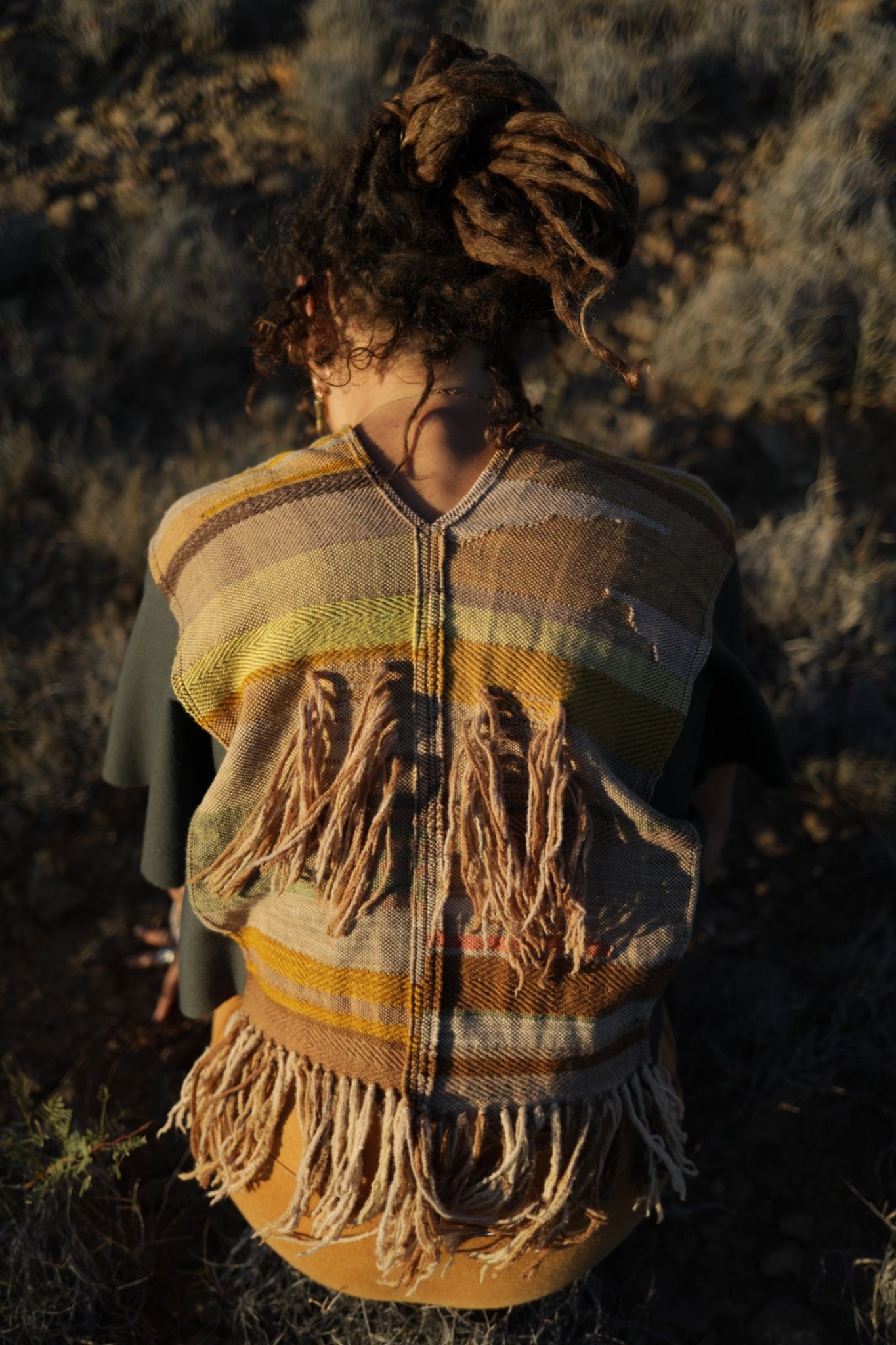 woman wearing brown, grey, red and yellow vest with fringe standing in the desert