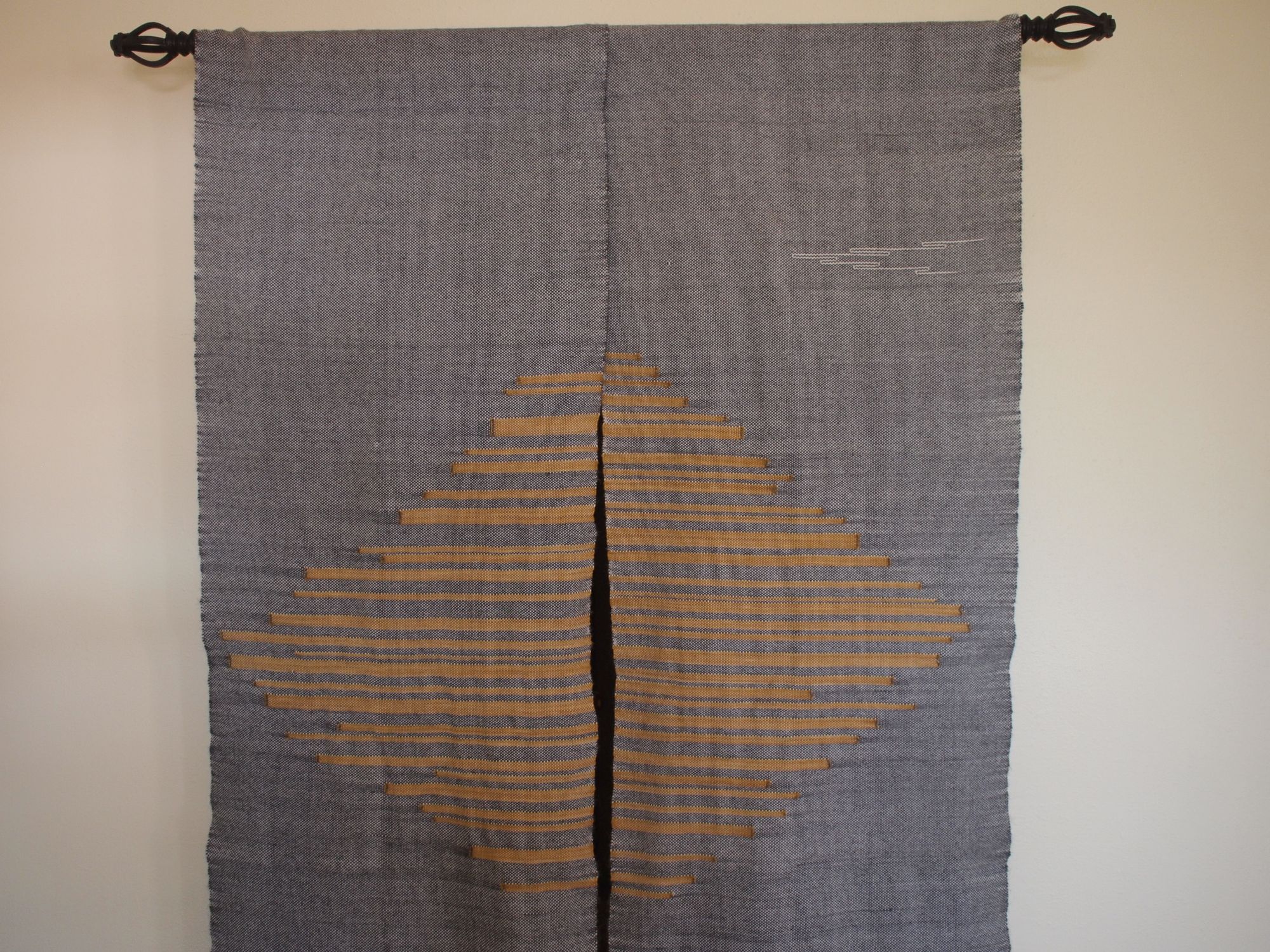 handwoven grey curtains with yellow sun-ray details hanging in a bedroom with white walls
