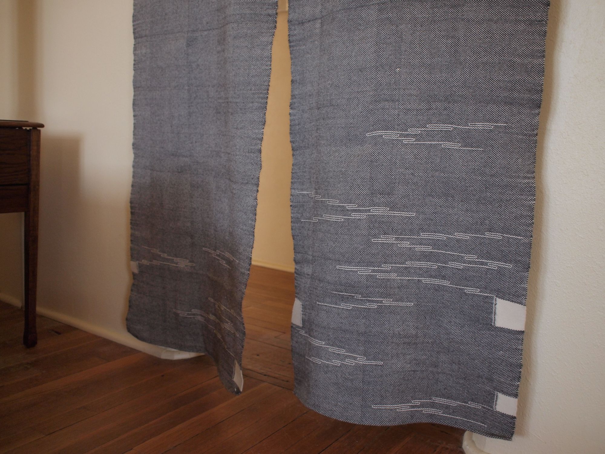 handwoven grey curtains with yellow sun-ray details hanging in a bedroom with white walls