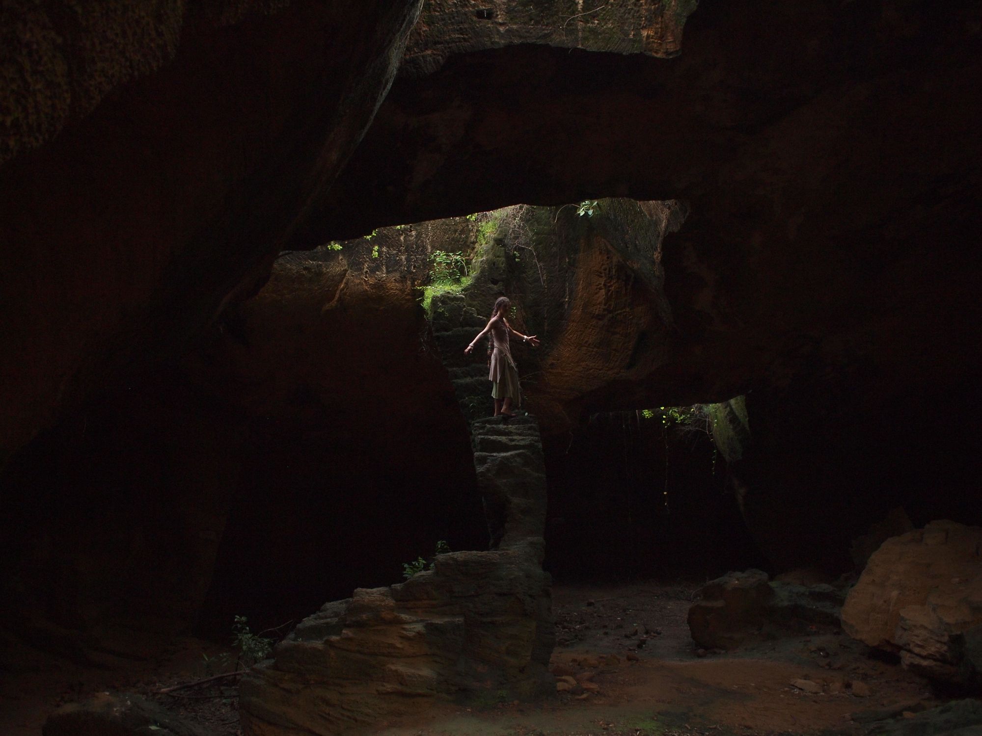 Woman standing in a cave, on steps carved out of stone. Light streams in from above. 