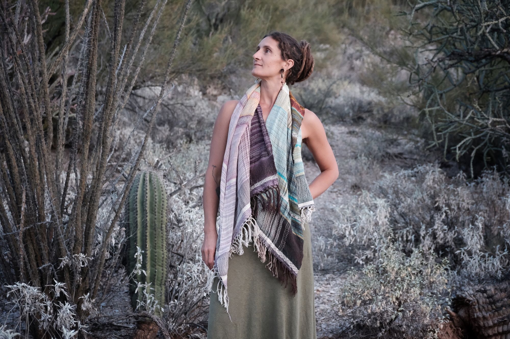 Woman wearing a blue, purple, white, brown and green scarf in the desert. 