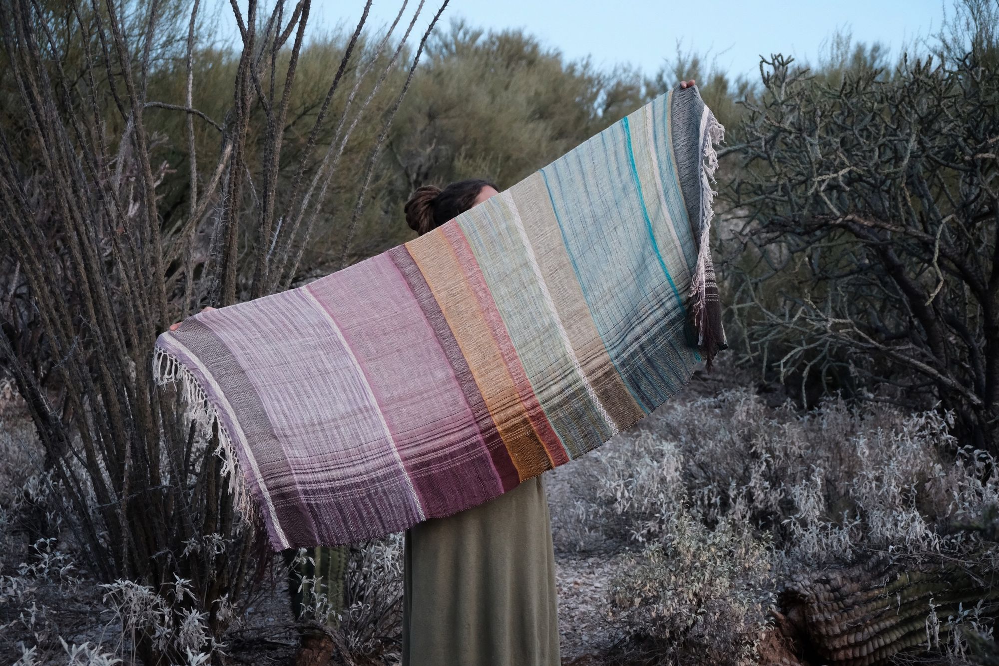 Woman wearing a blue, purple, white, brown and green scarf in the desert. 