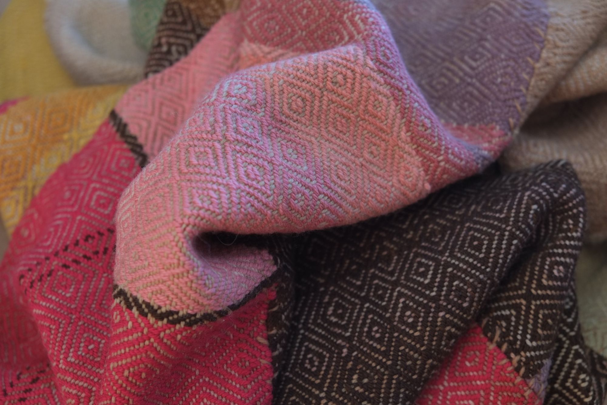 Details of a brown, pink, yellow, blue, green, tan and purple woolen blanket with a diamond pattern.