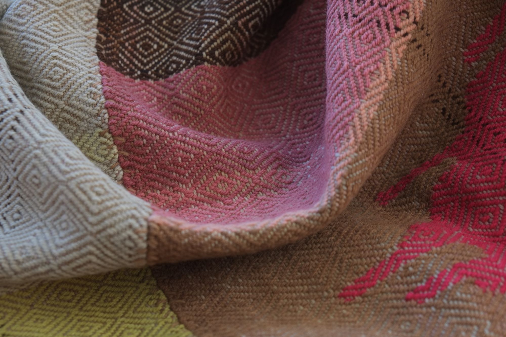 Details of a brown, pink, yellow, blue, green, tan and purple woolen blanket with a diamond pattern.