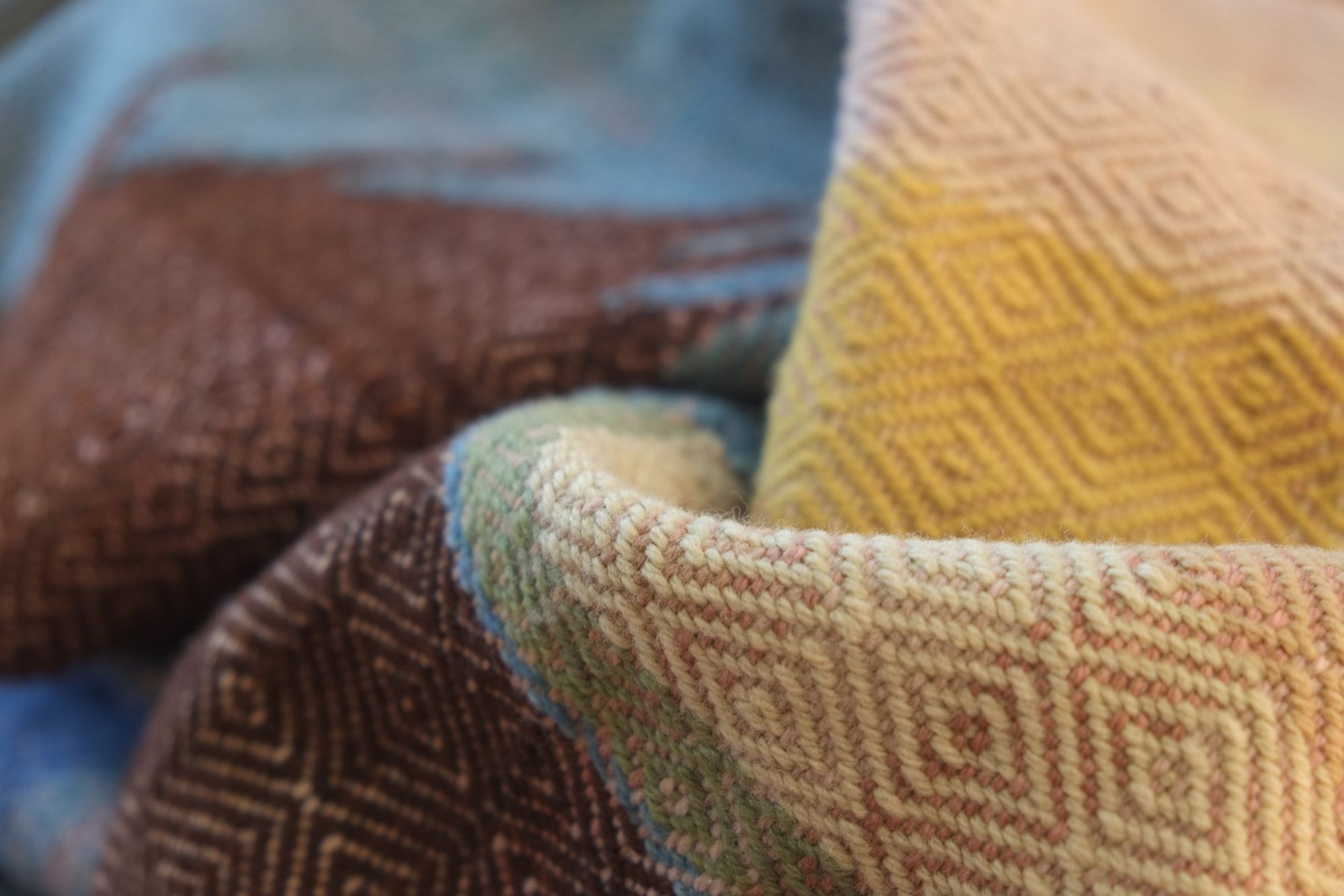 Details of a brown, pink, yellow, blue, green, tan and purple woolen blanket with a diamond pattern.