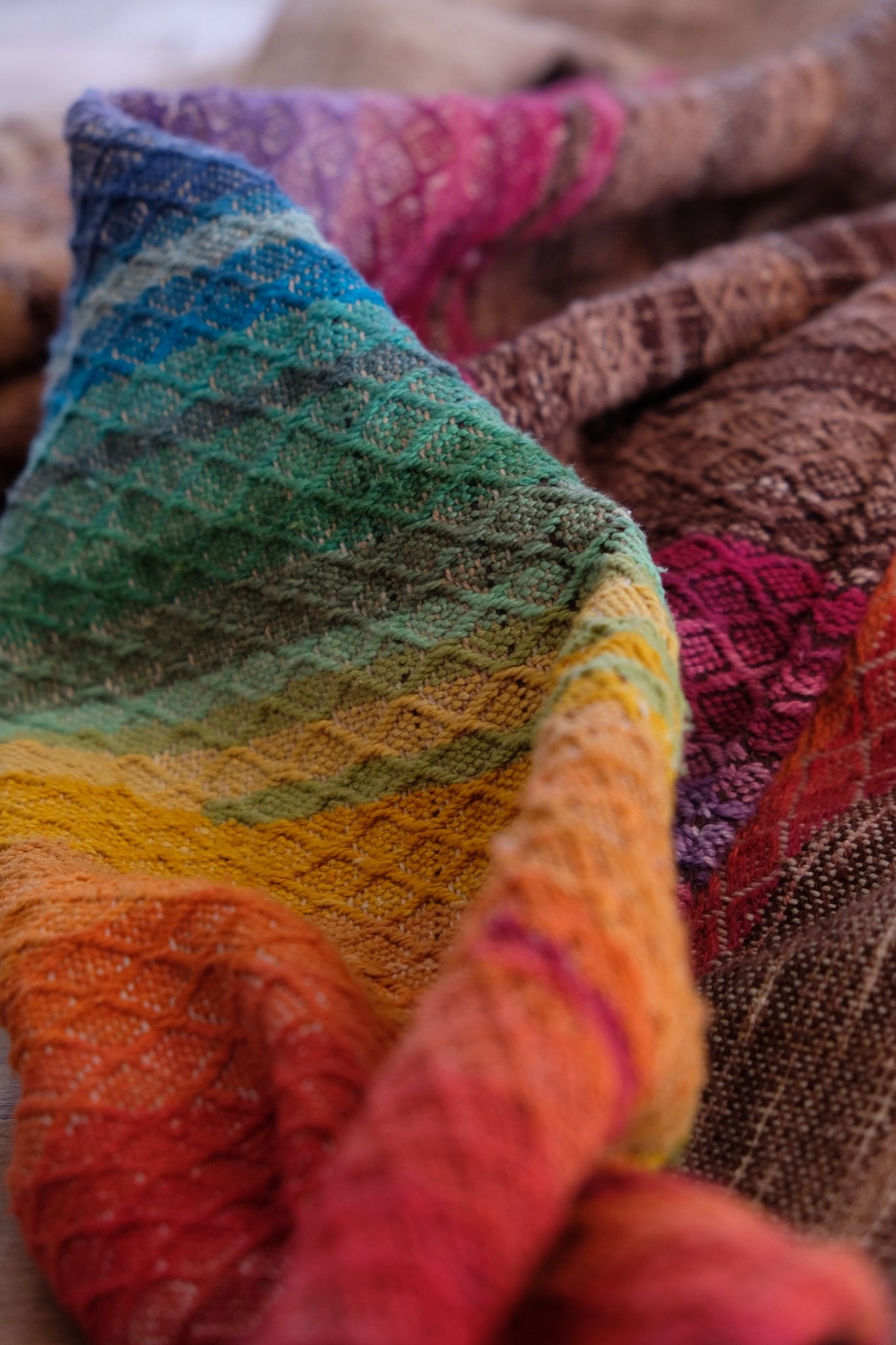 detail of handwoven fabric with textured diamond weave in rainbow colors with browns and tans