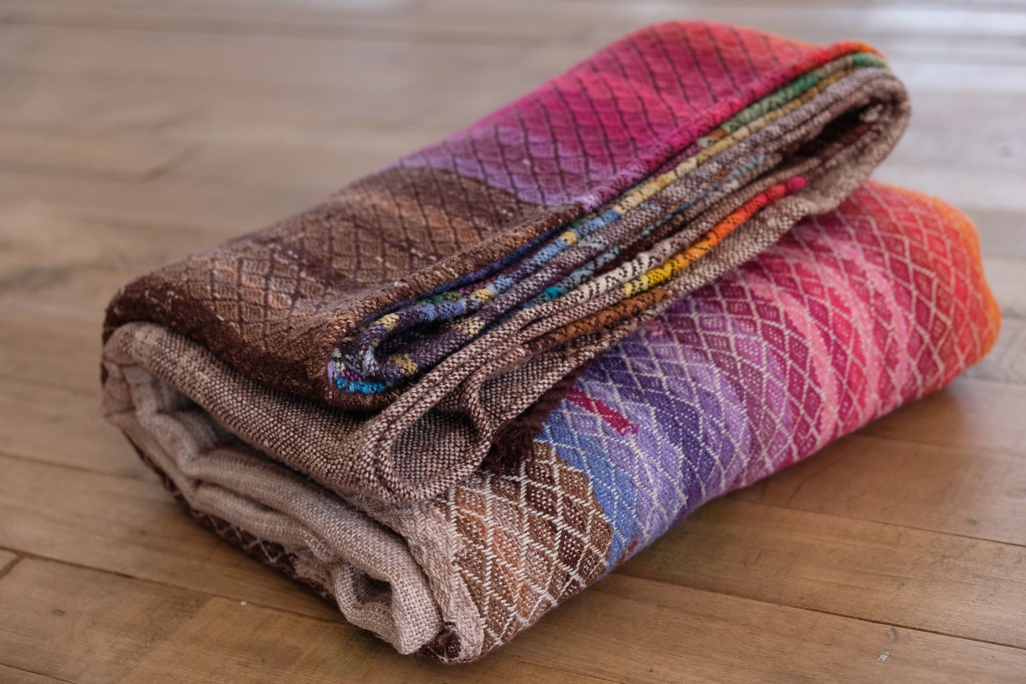 folded on a wooden floor Handwoven, highly textures Diamond pattern fabric in every color of the rainbow, with natural browns and tans