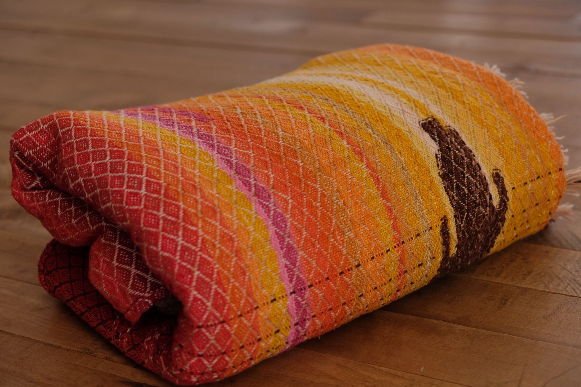 folded, and sitting on a wooden floor Handwoven, highly textures Diamond pattern fabric in every color of the rainbow, with natural browns and tans