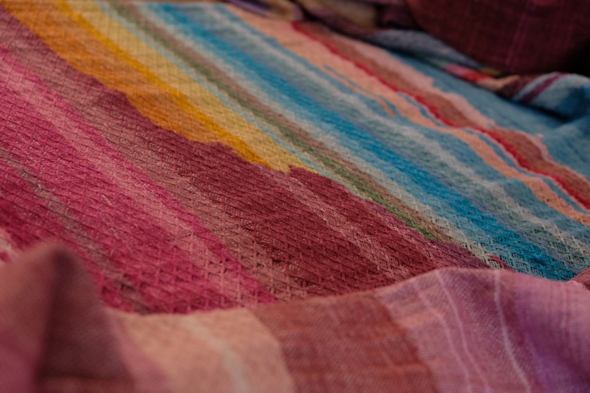 Brightly colored fabric in pink, yellow, orange, blue, cream, green and purple is laid out on a wooden floor