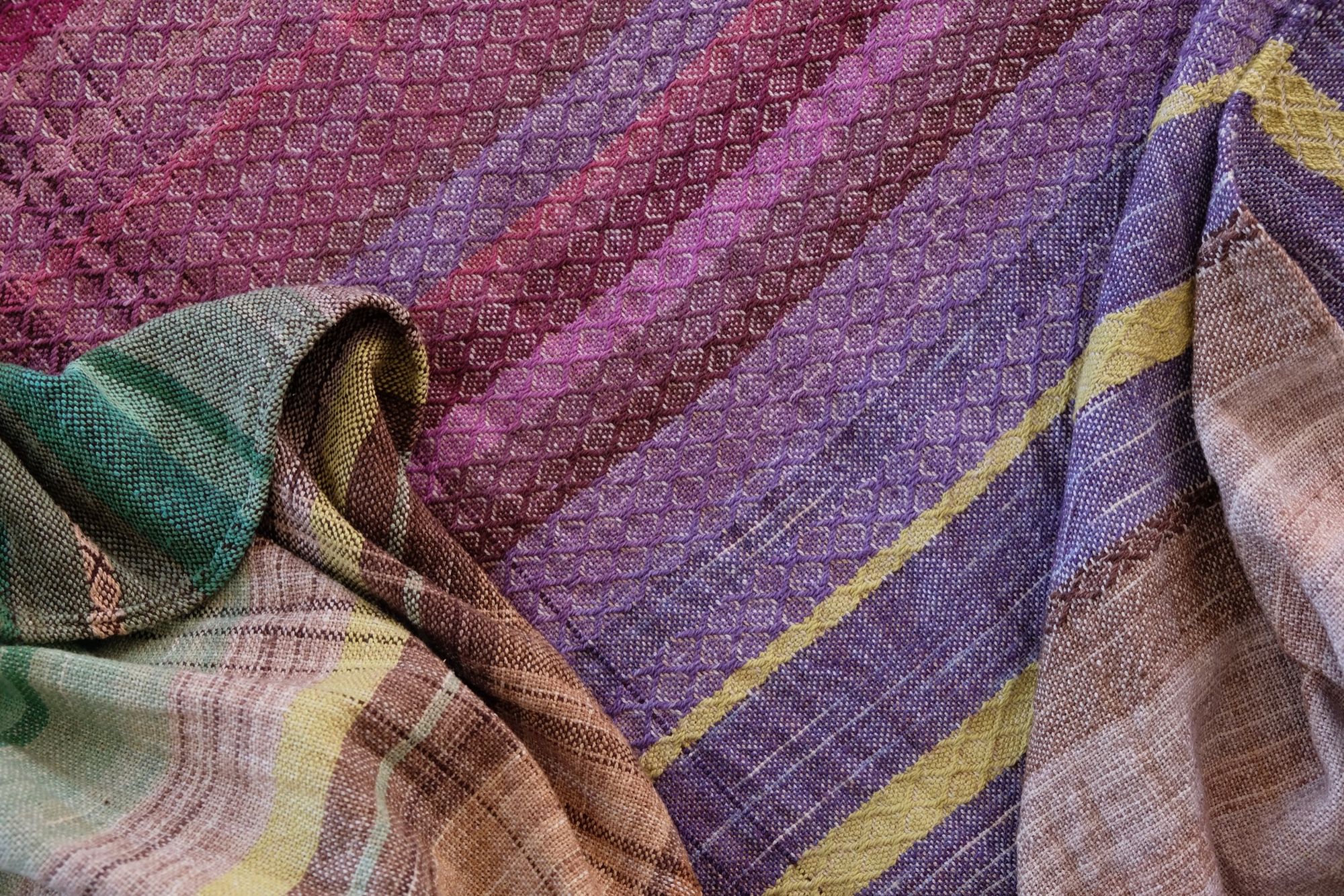 detail of Handwoven raw silk fabric with textures diamond weave in browns, tans, purples, blues, yellows, pink and orange laying on a wooden floor