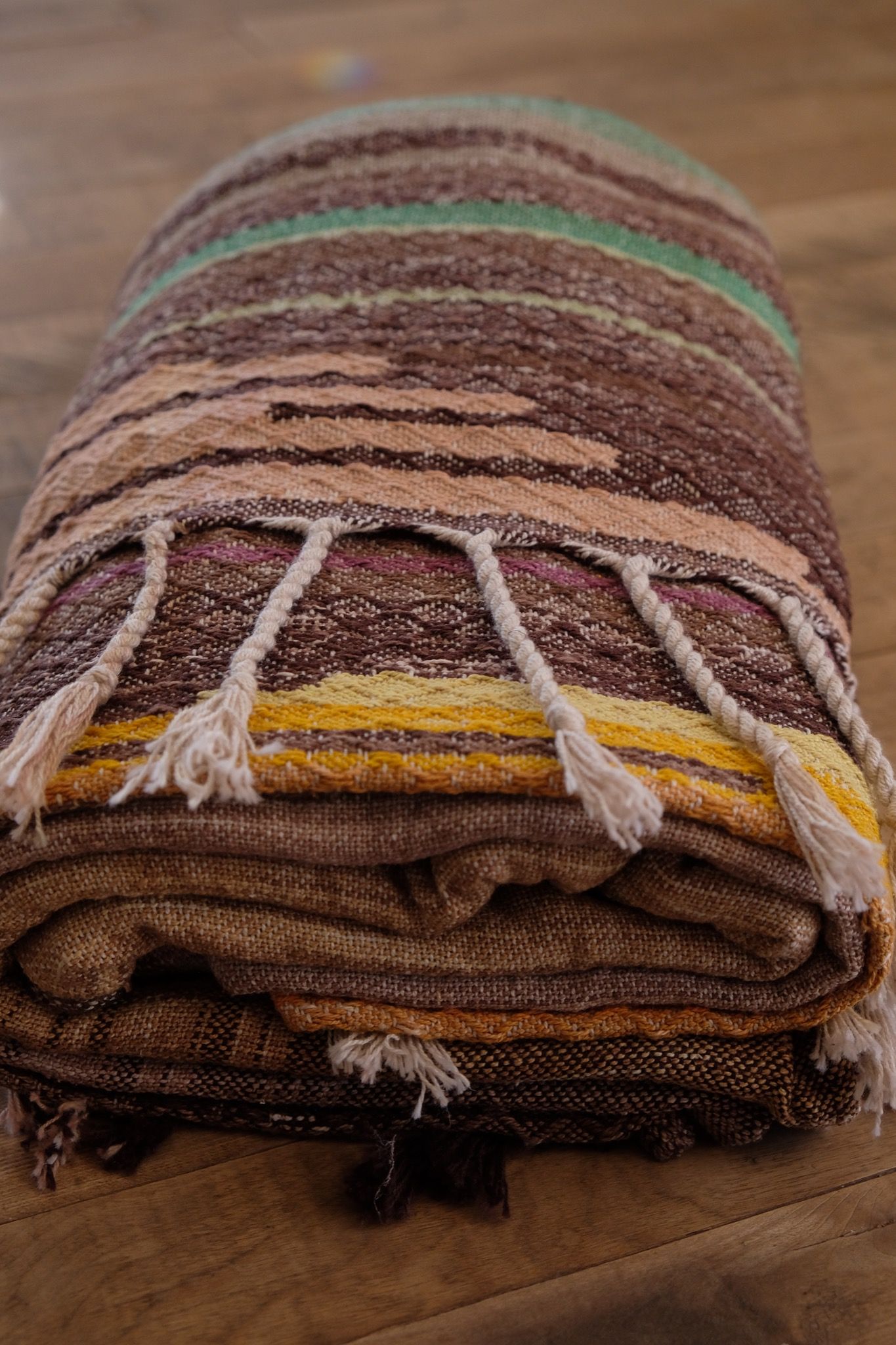 detail of Handwoven raw silk fabric with textures diamond weave in browns, tans, purples, blues, yellows, pink and orange laying on a wooden floor