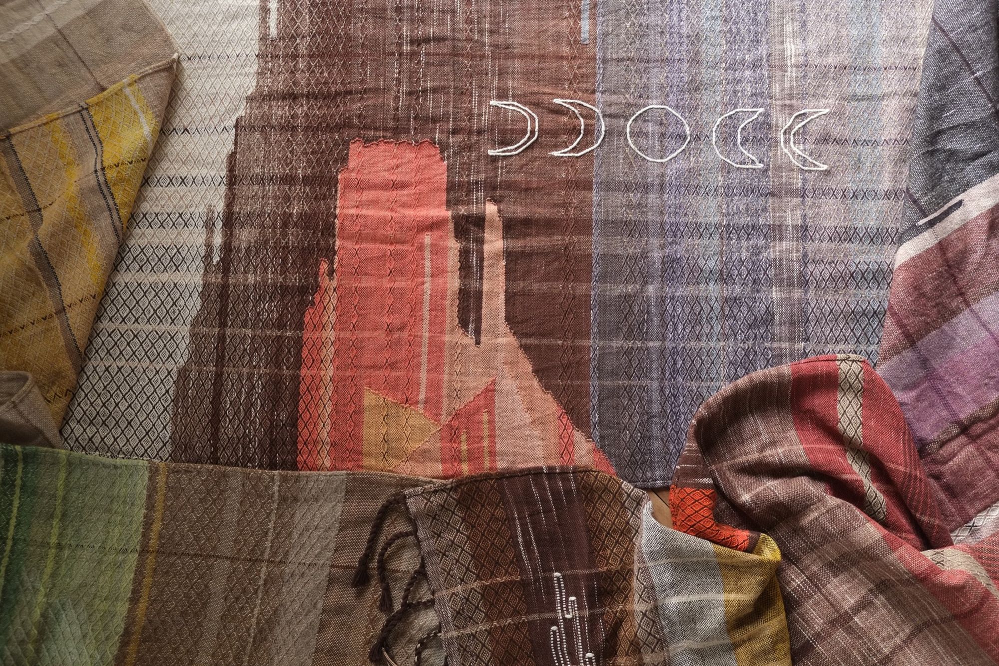 Handwoven fabric with the moon phases and salmon colored stone-shapes woven into it on a background of blue and brown
