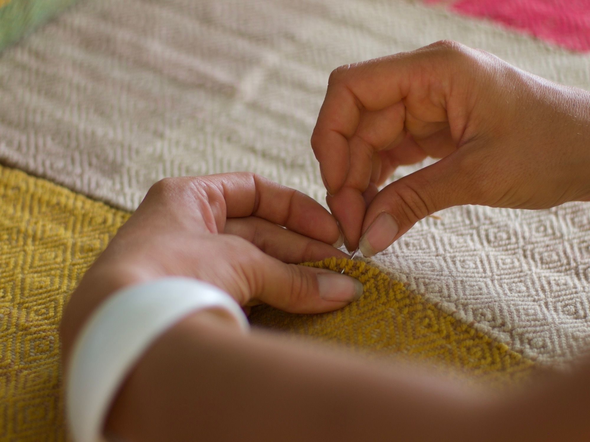 Hands sewing together two panels of fabric, one white, one yellow