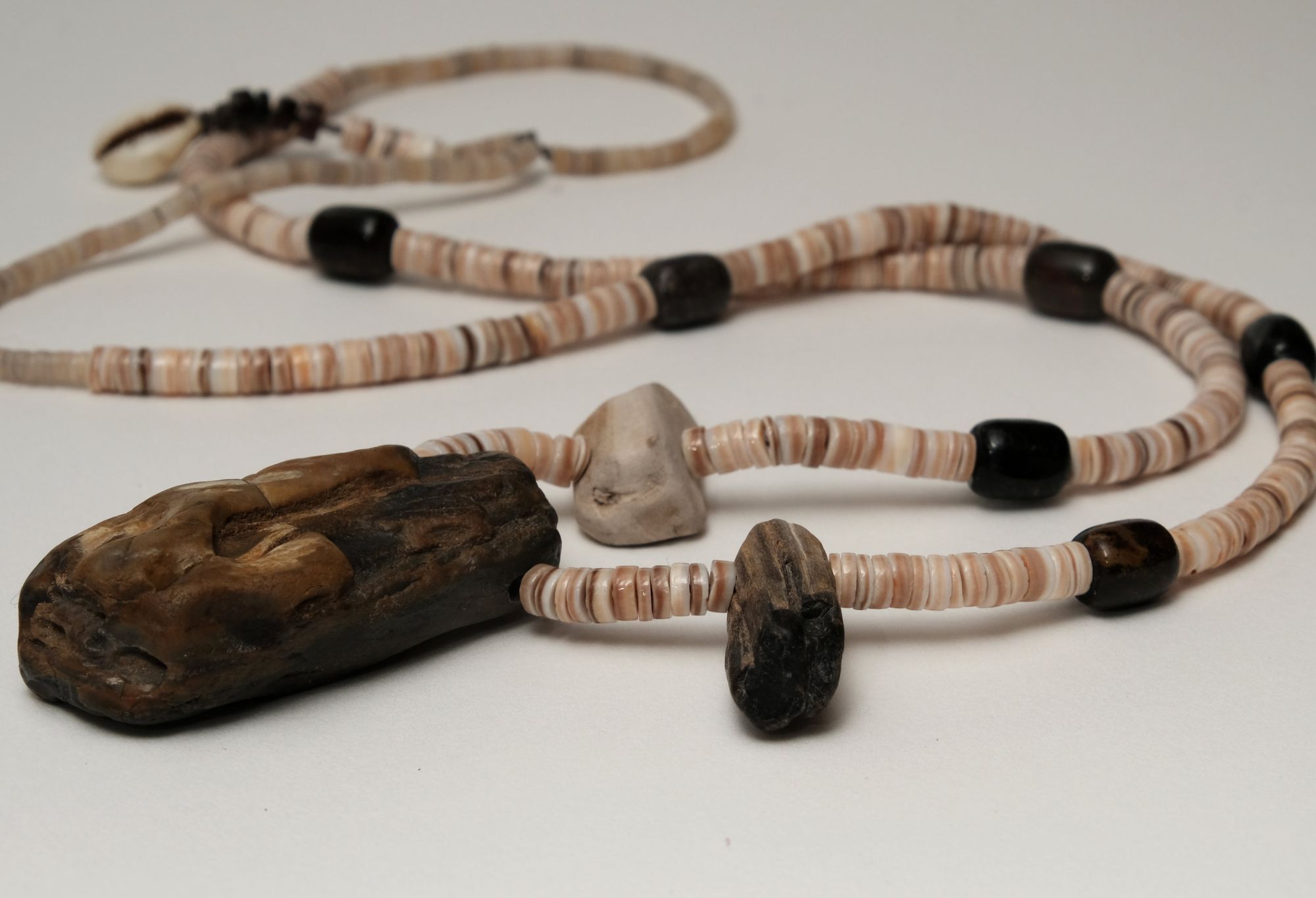 tan and brown shell, black fossil and earth tone petrified wood necklace laying on a white backdrop 