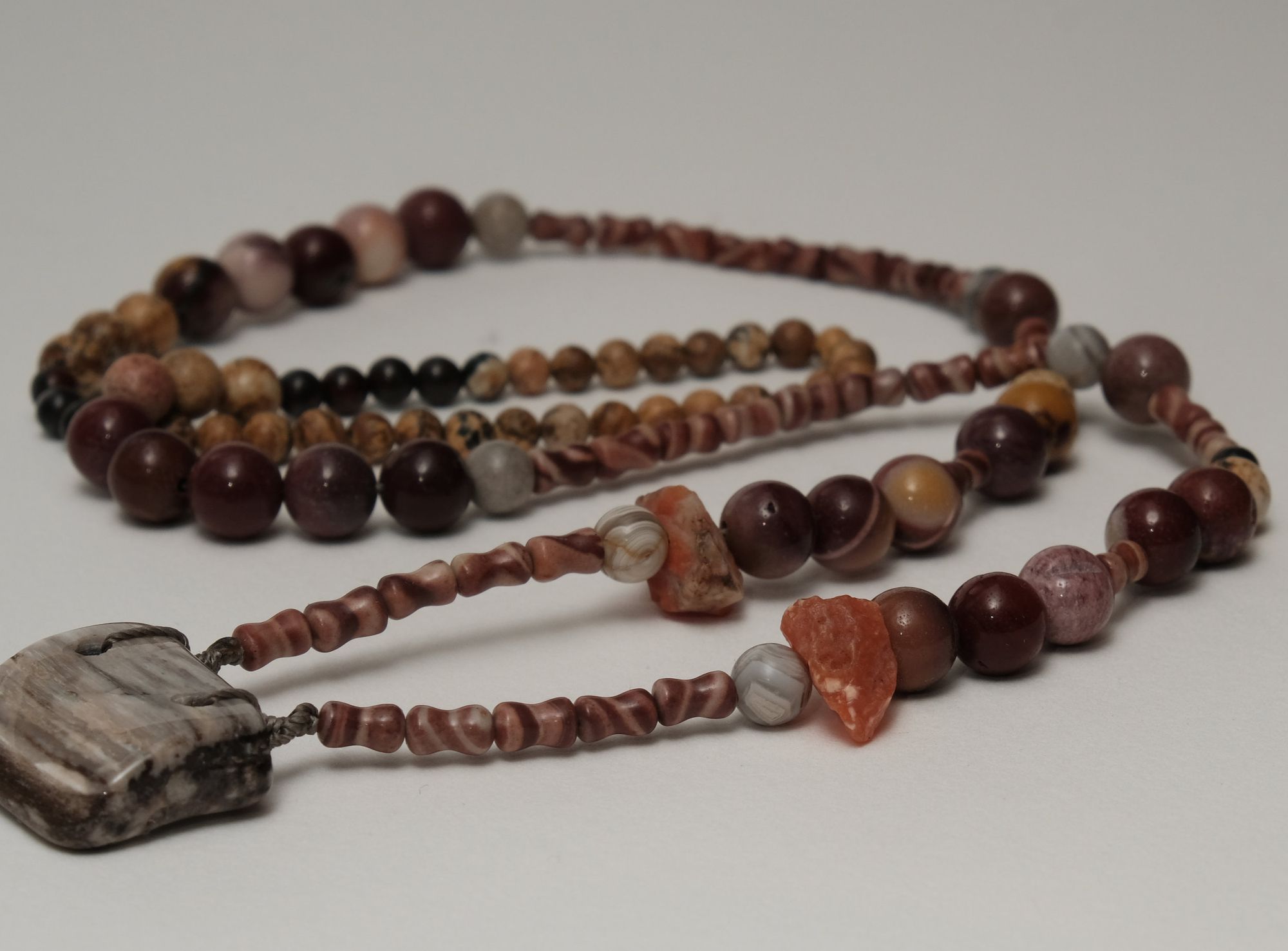 multicolored rough stone and petrified wood necklace laying on a white backdrop