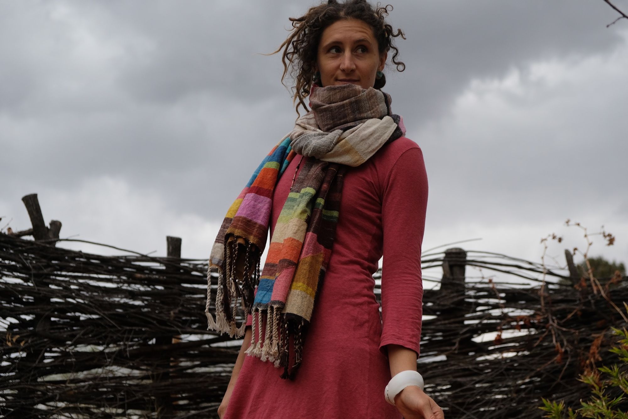 woman wearing a many colored handwoven shawl in front of a stick fence
