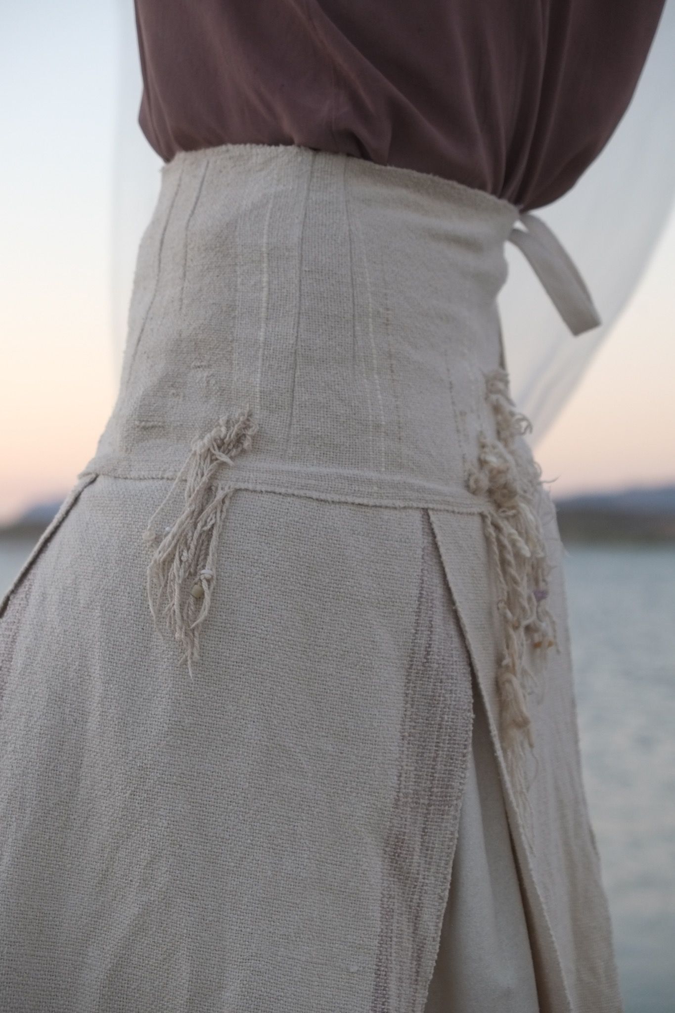 woman wearing white wedding skirt and lilac shirt by a still lake at sunset