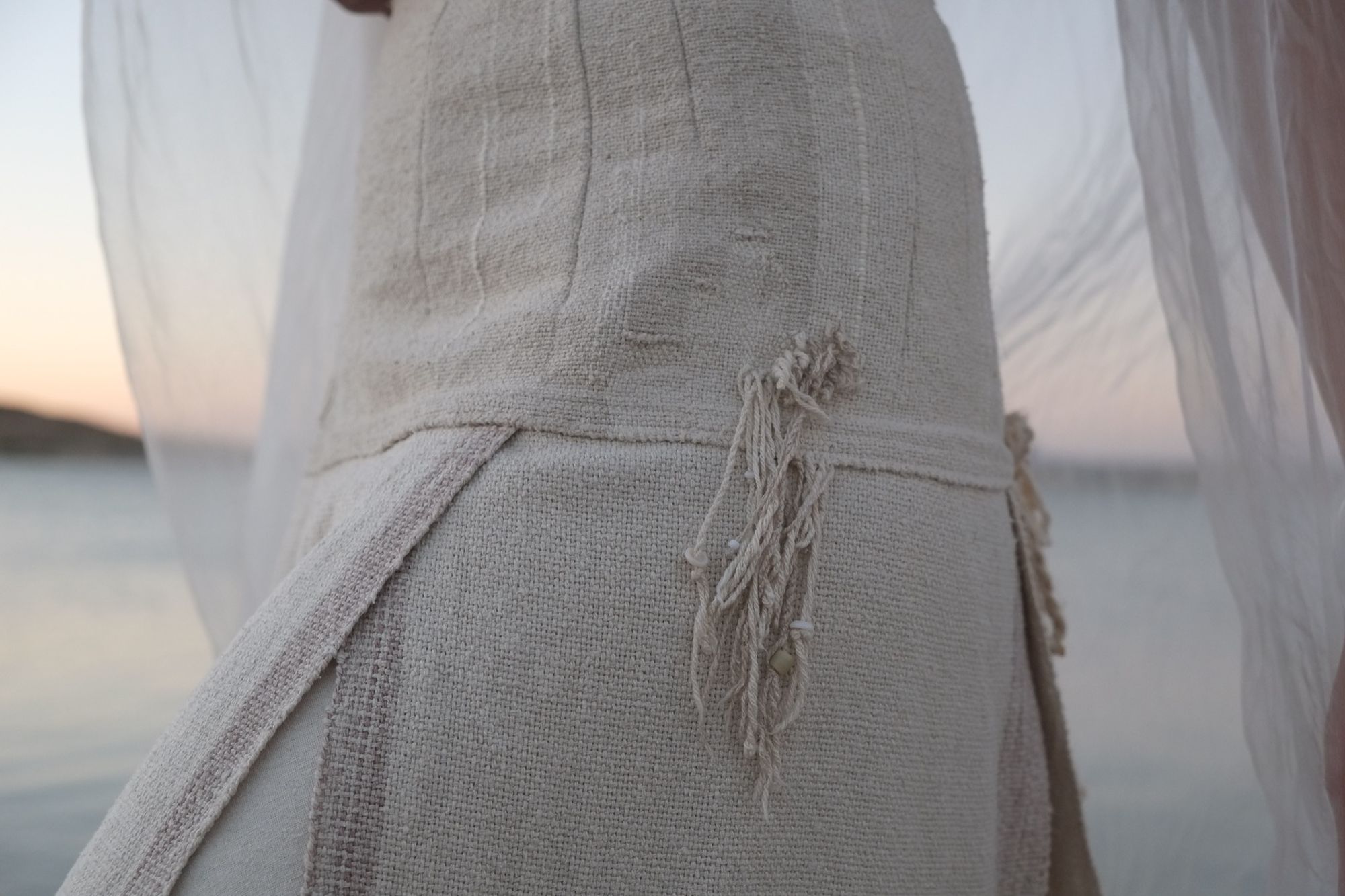 woman wearing white wedding skirt and lilac shirt by a still lake at sunset