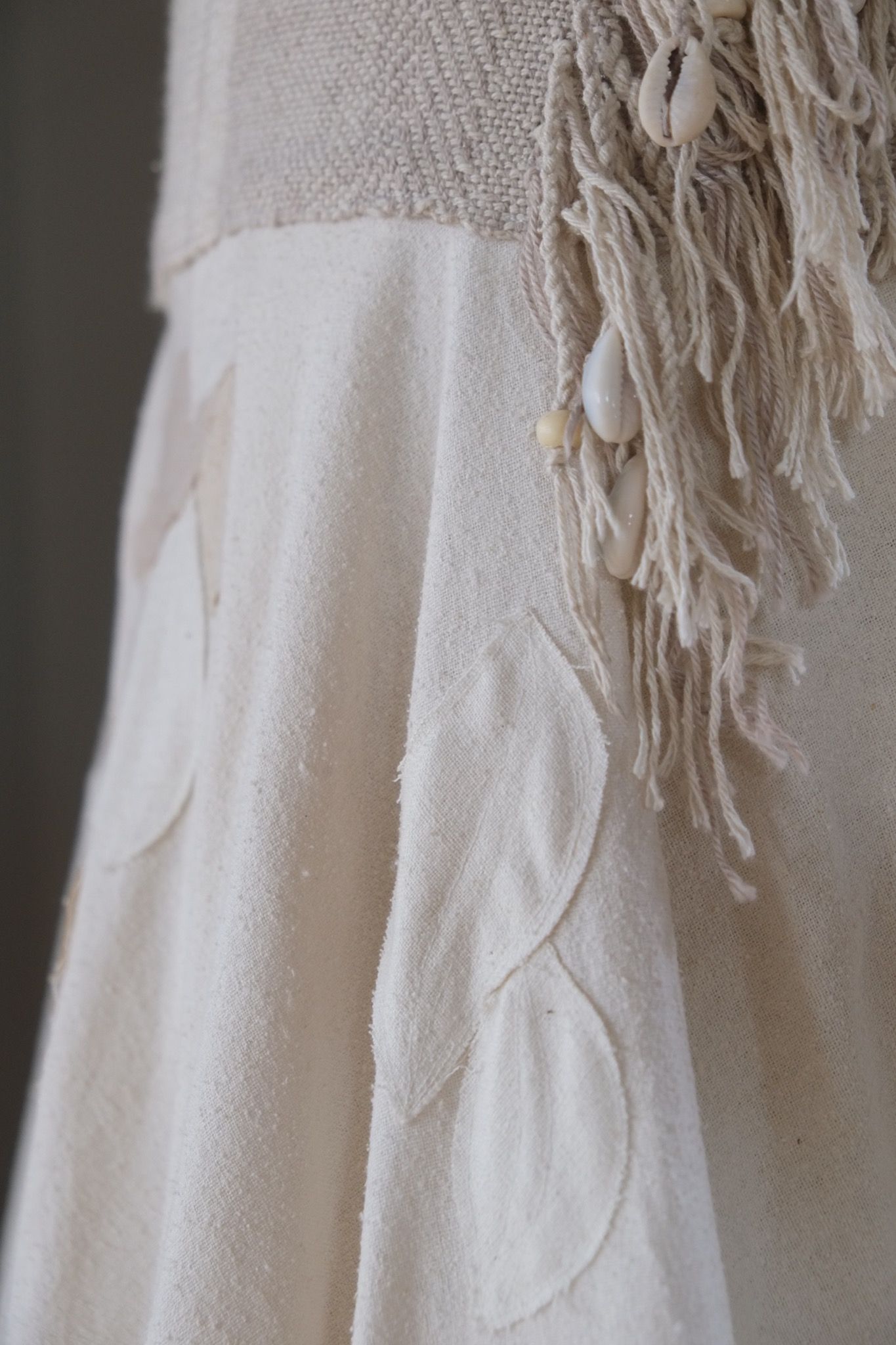 detail of a white handmade wedding skirt with handwoven waistband, fringe and leaf applique
