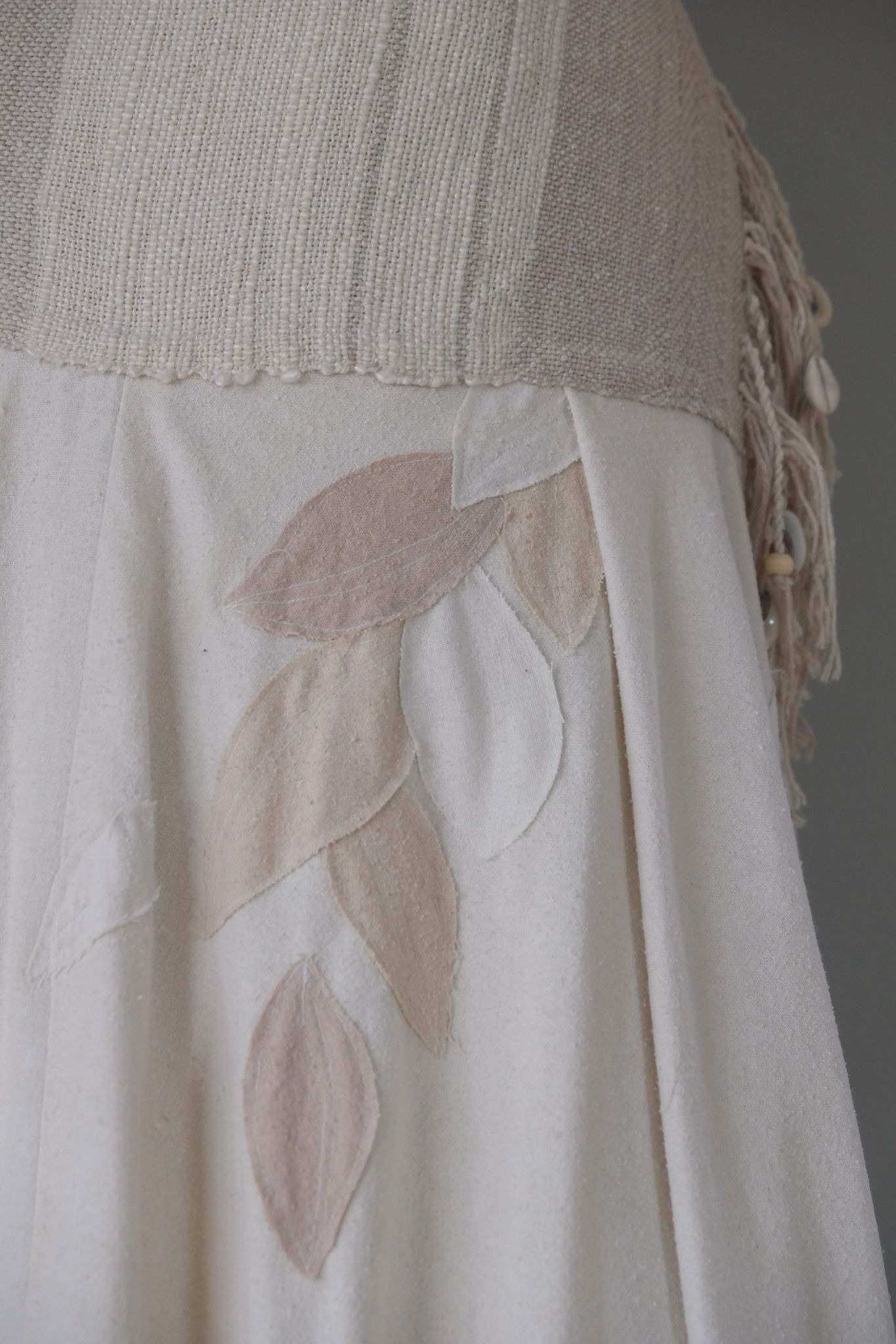 detail of a white handmade wedding skirt with handwoven waistband, fringe and leaf applique