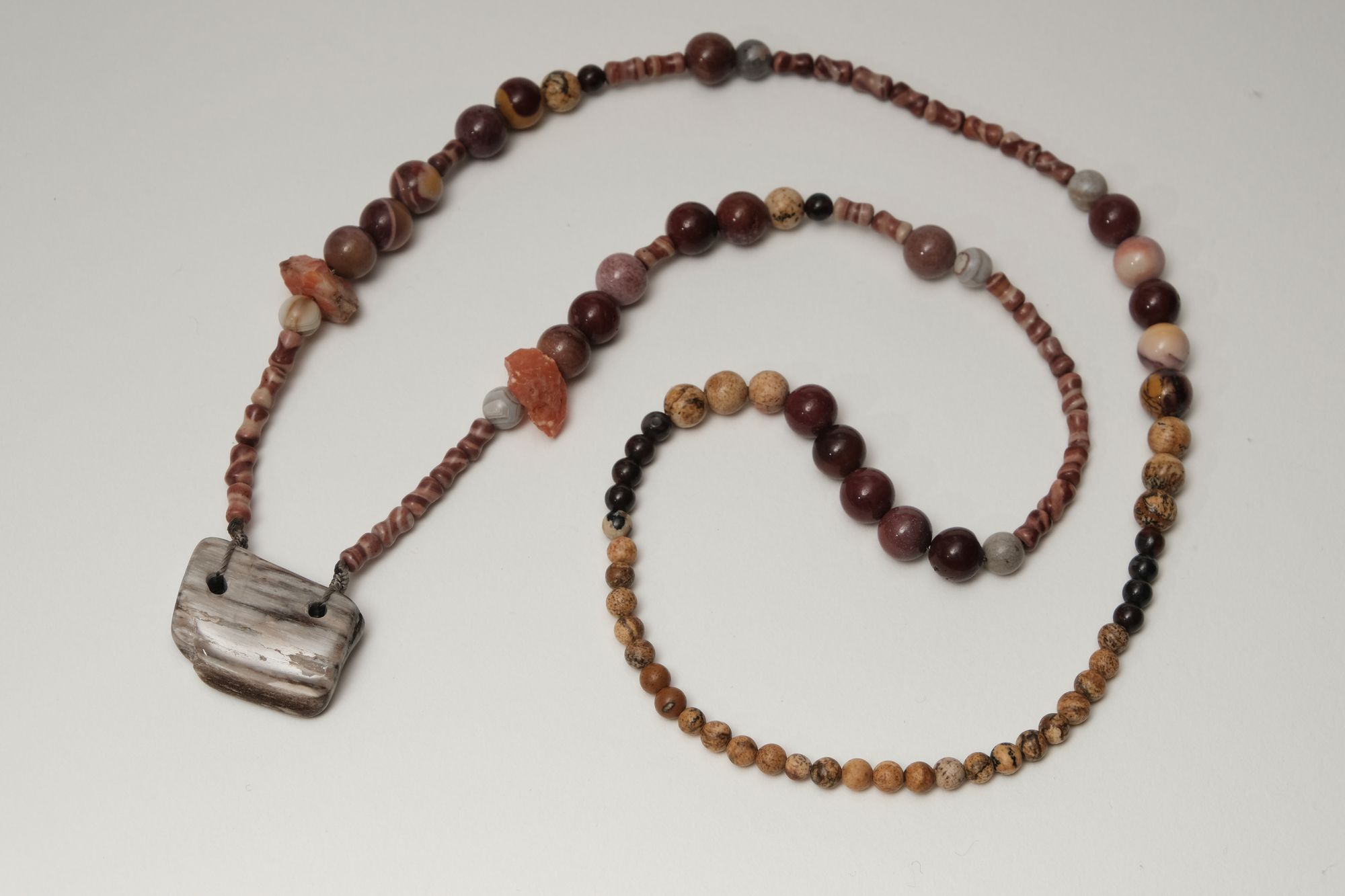multicolored rough stone and petrified wood necklace laying on a white backdrop