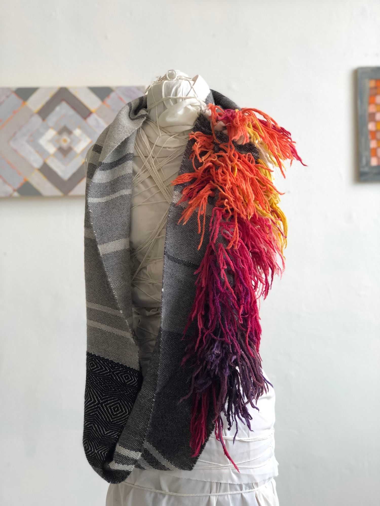 rainbow fringe, grey, black and white handwoven cowl scarf with fringe on a white mannequin in a white walled gallery