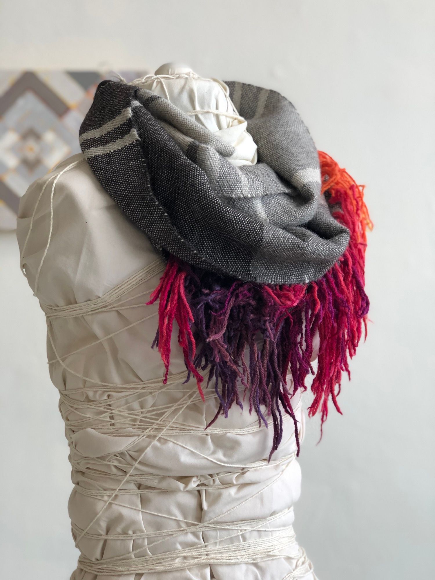 rainbow fringe, grey, black and white handwoven cowl scarf with fringe on a white mannequin in a white walled gallery