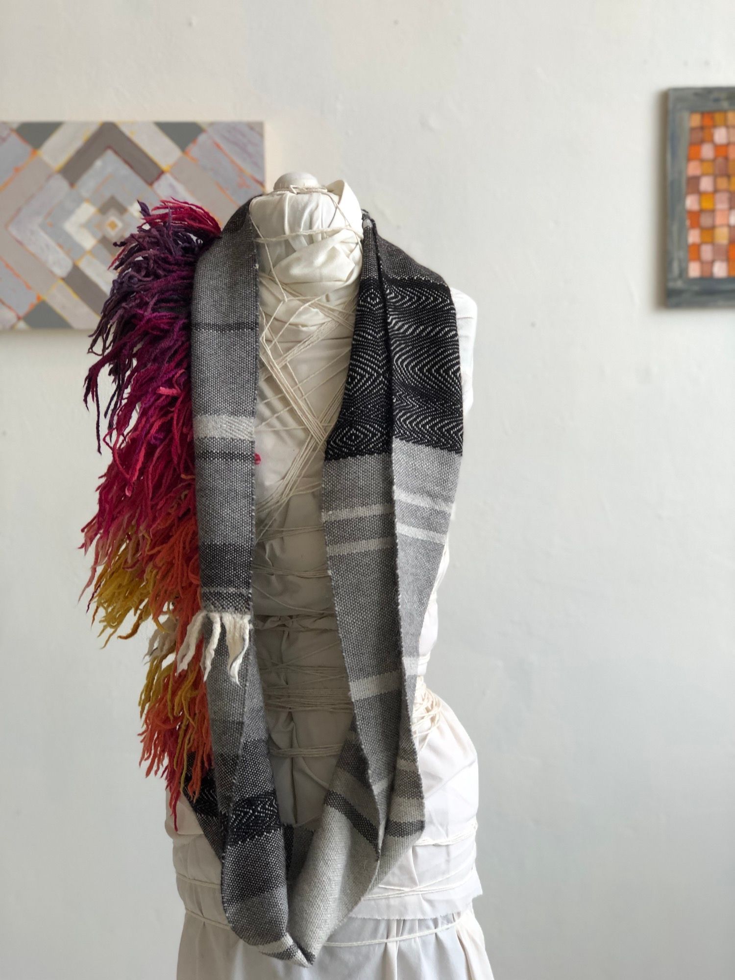 rainbow fringe, grey, black and white handwoven cowl scarf with fringe on a white mannequin in a white walled gallery