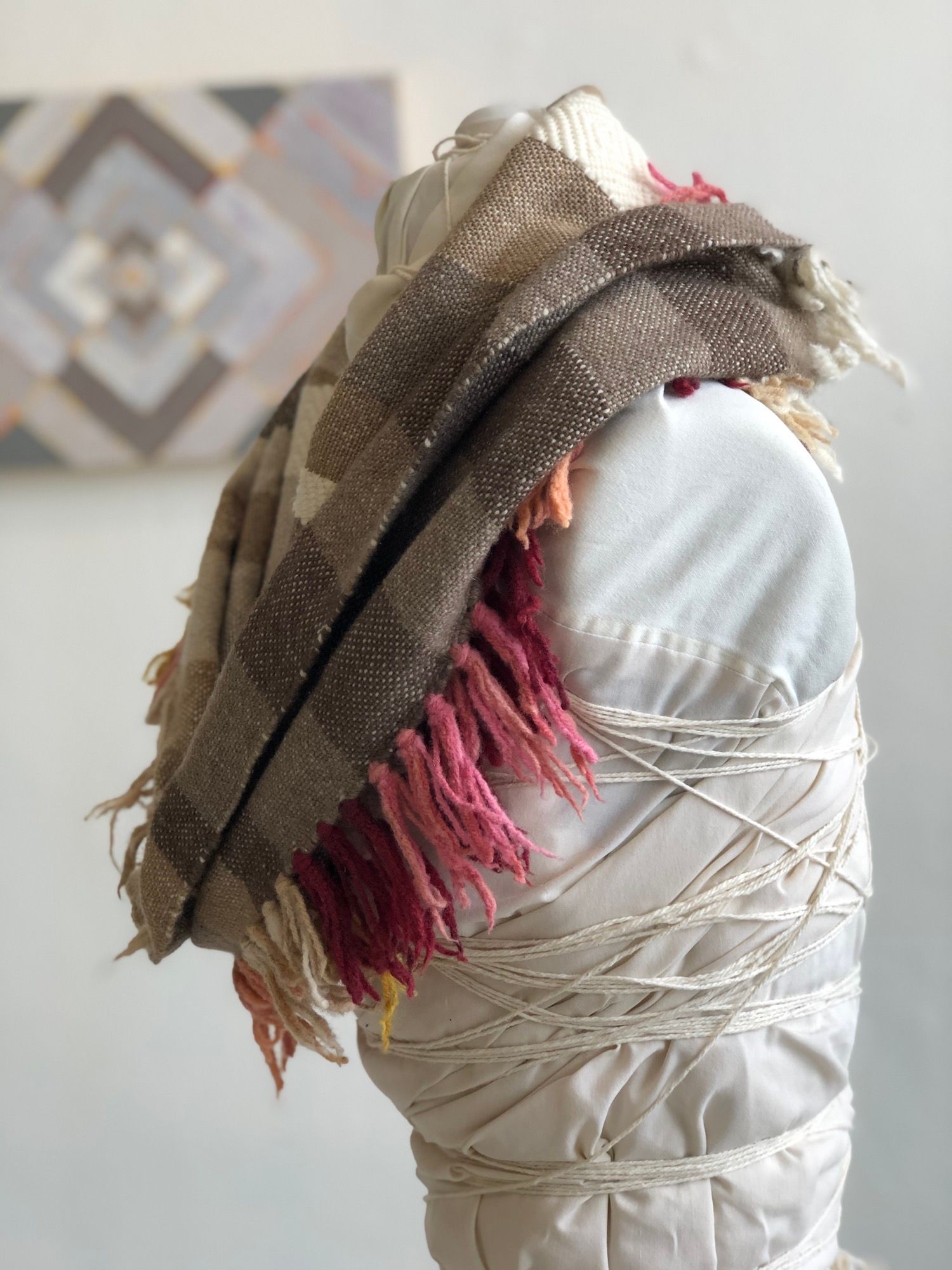 grey, brown, rainbow and  white handwoven cowl scarf with fringe on a white mannequin in a white walled gallery