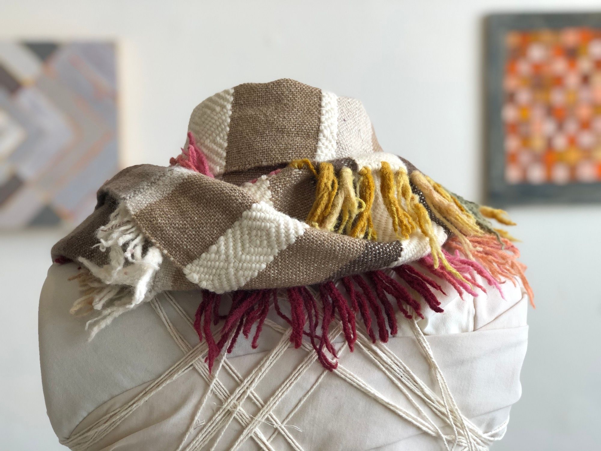 grey, brown, rainbow and  white handwoven cowl scarf with fringe on a white mannequin in a white walled gallery