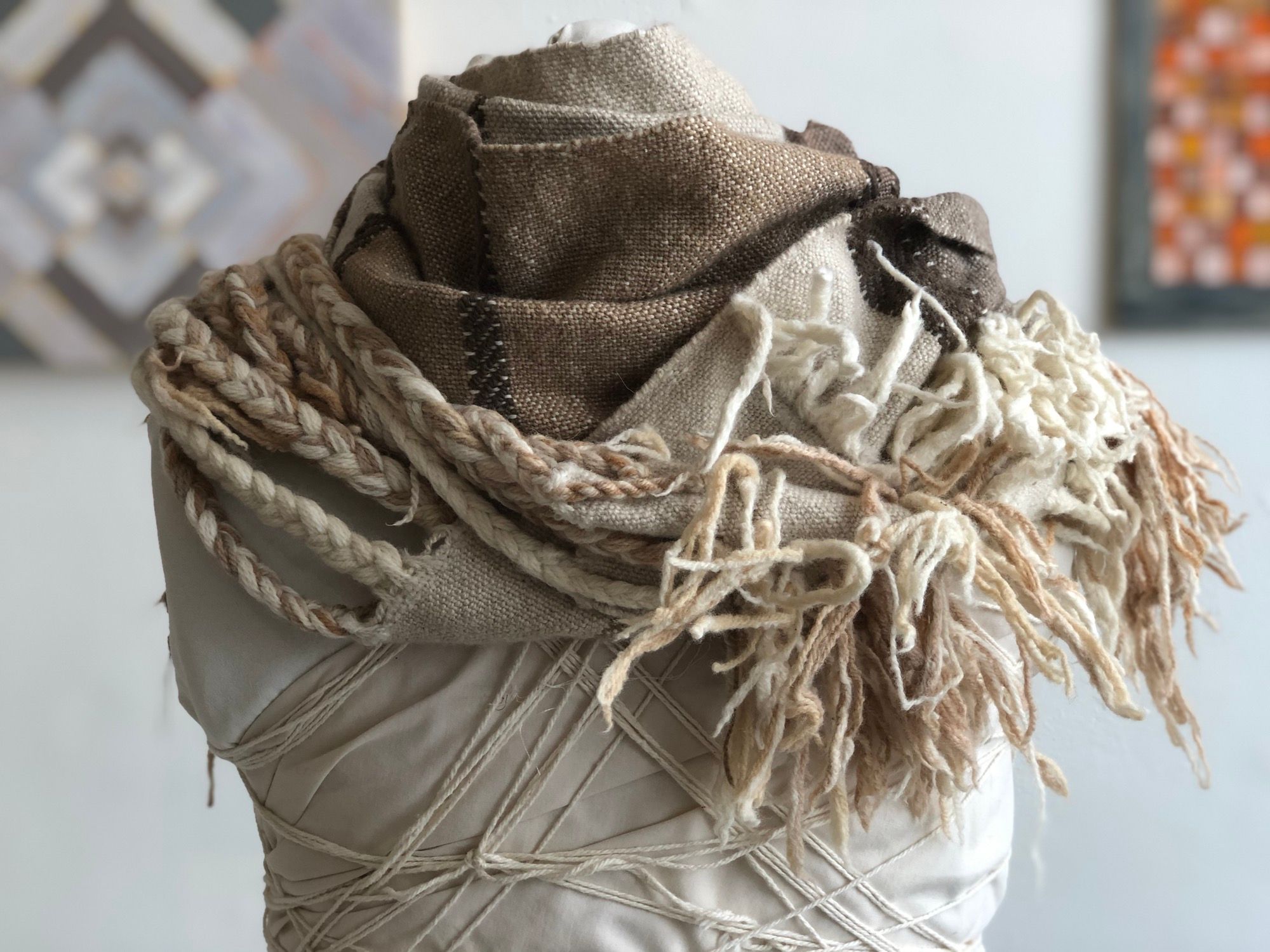 brown, grey, tan and white handwoven cowl scarf with fringe on a white mannequin in a white walled gallery