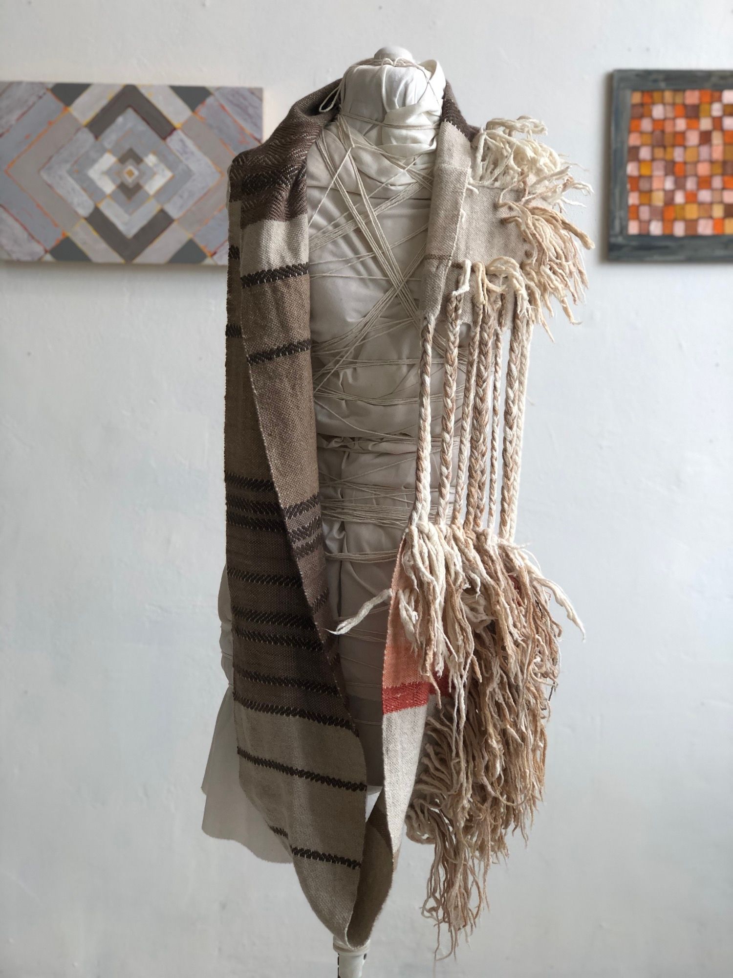 brown, grey, tan and white handwoven cowl scarf with fringe on a white mannequin in a white walled gallery