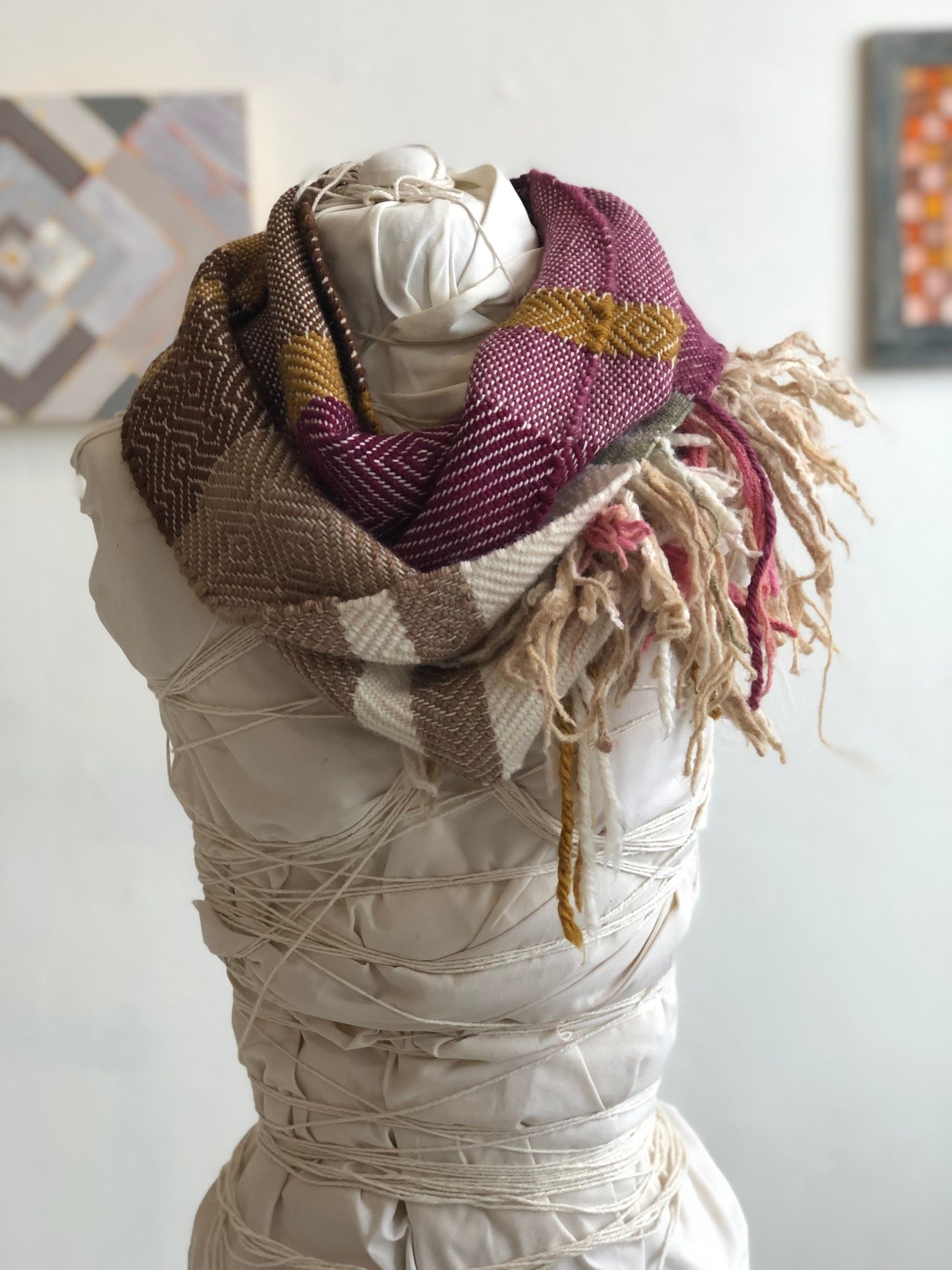 brown, yellow, tan and raspberry handwoven cowl scarf with fringe on a white mannequin in a white walled gallery
