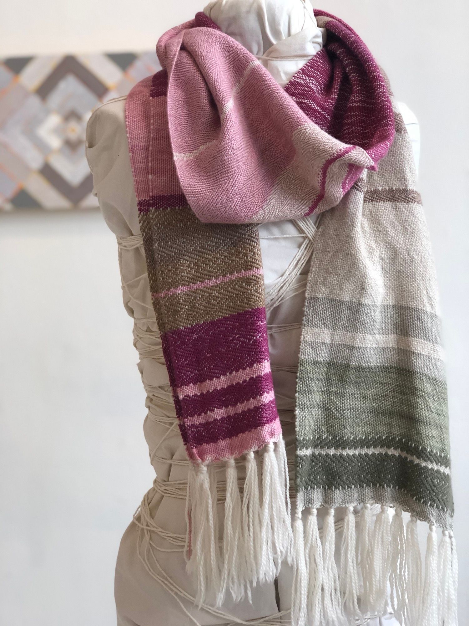 raspberry pink, brown, grey and white handwoven scarf with fringe on a white mannequin in a white walled gallery