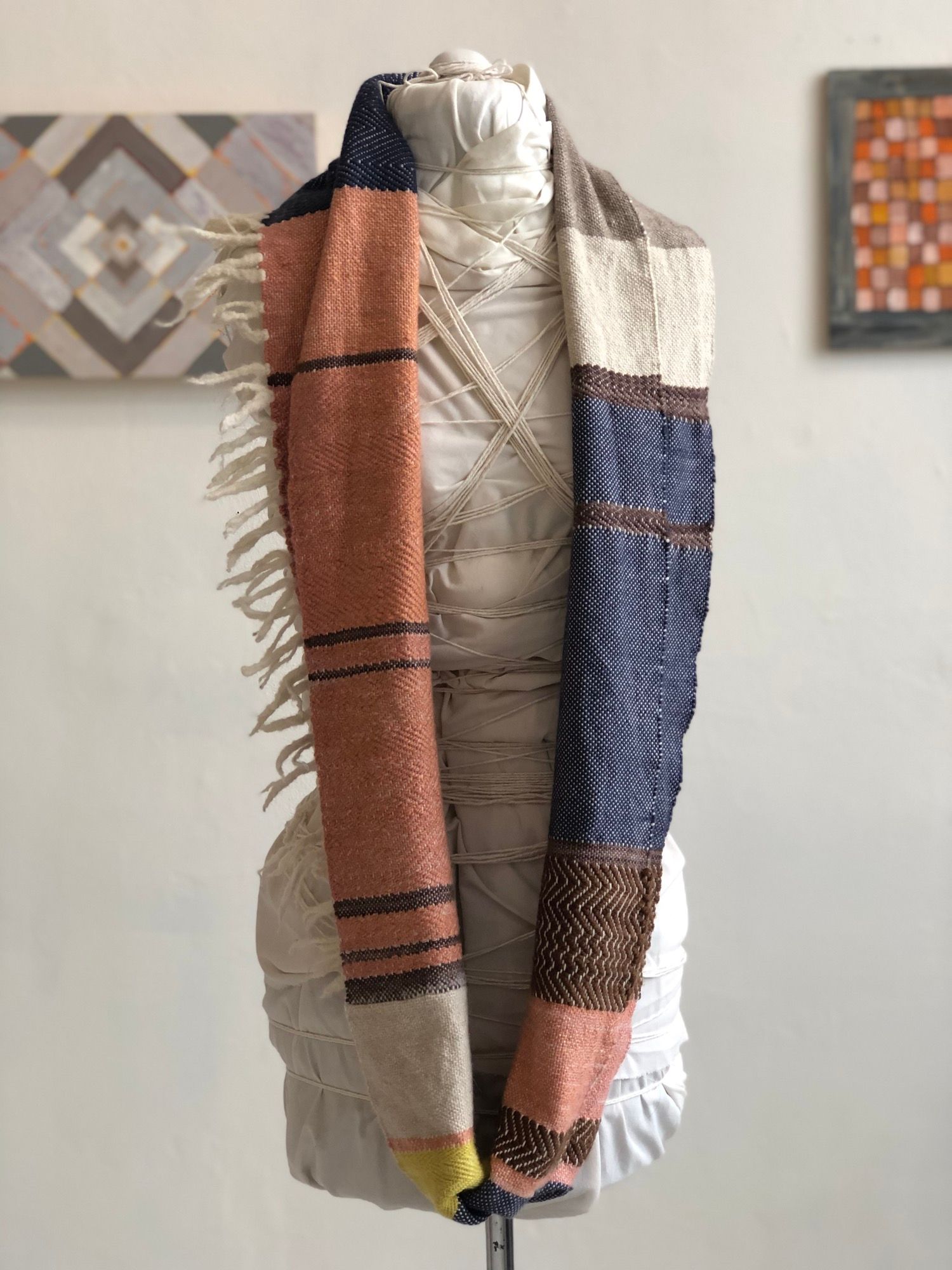 salmon, purple, brown, yellow and white handwoven cowl scarf with fringe on a white mannequin in a white walled gallery