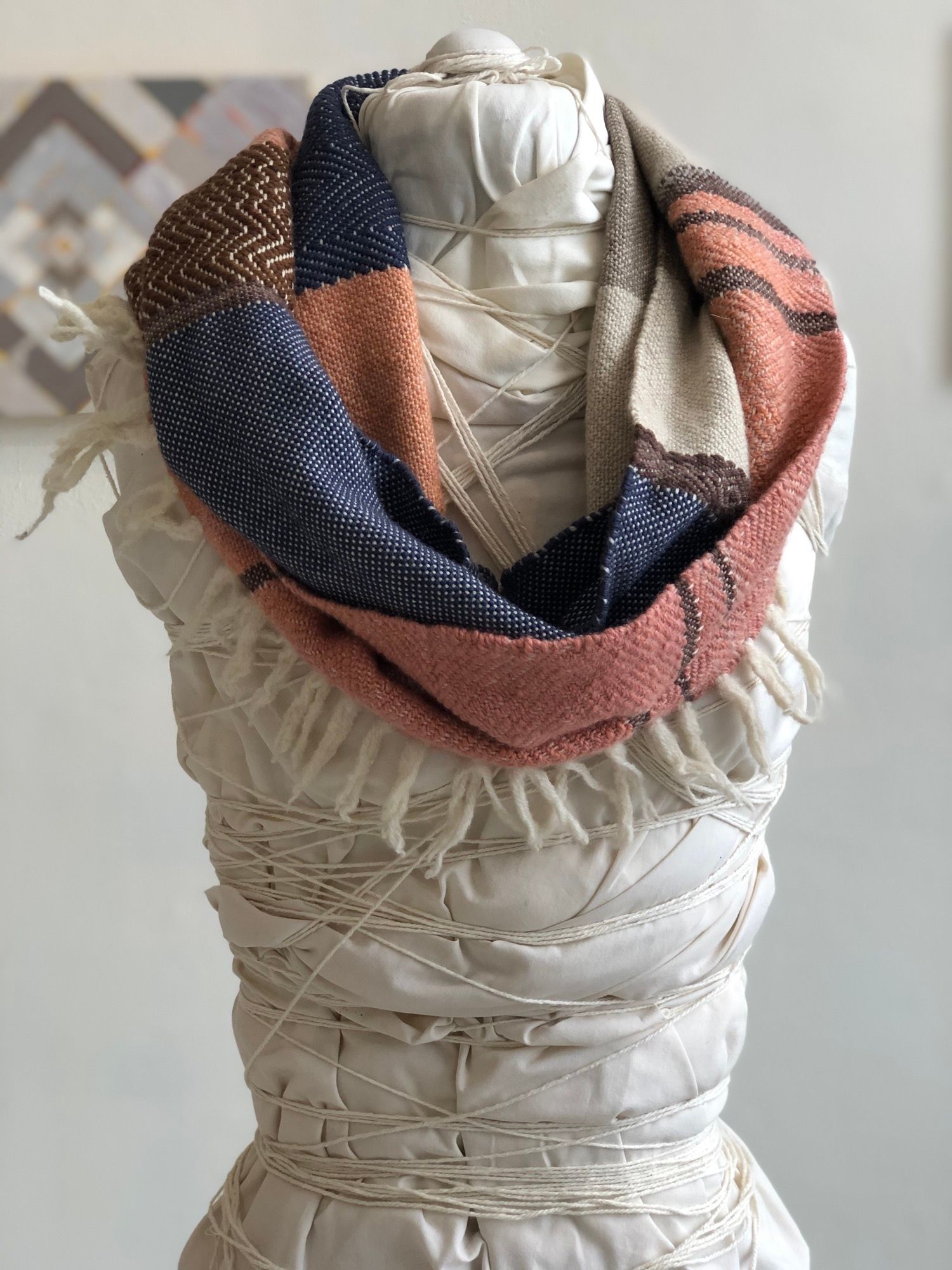 salmon, purple, brown, yellow and white handwoven cowl scarf with fringe on a white mannequin in a white walled gallery