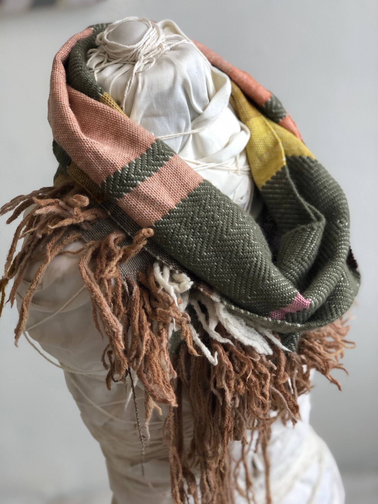 peach, yellow, green, pink and brown handwoven textured cowl scarf on a white mannequin in a white room
