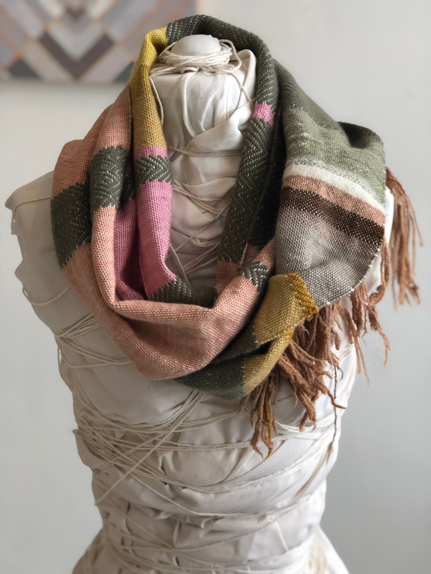 peach, yellow, green, pink and brown handwoven textured cowl scarf on a white mannequin in a white room