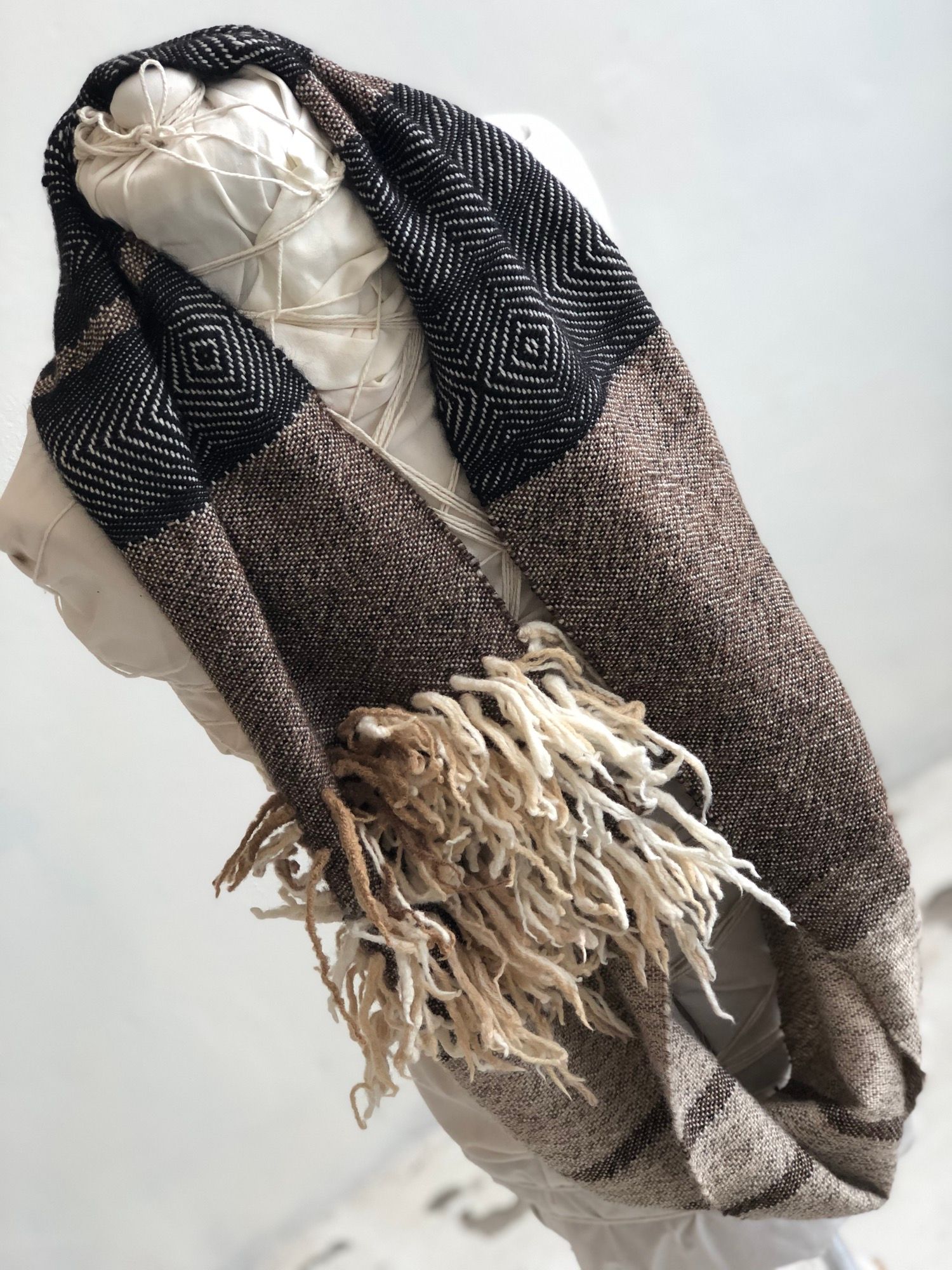 brown, grey, black and white handwoven cowl scarf with fringe on a white mannequin in a white walled gallery