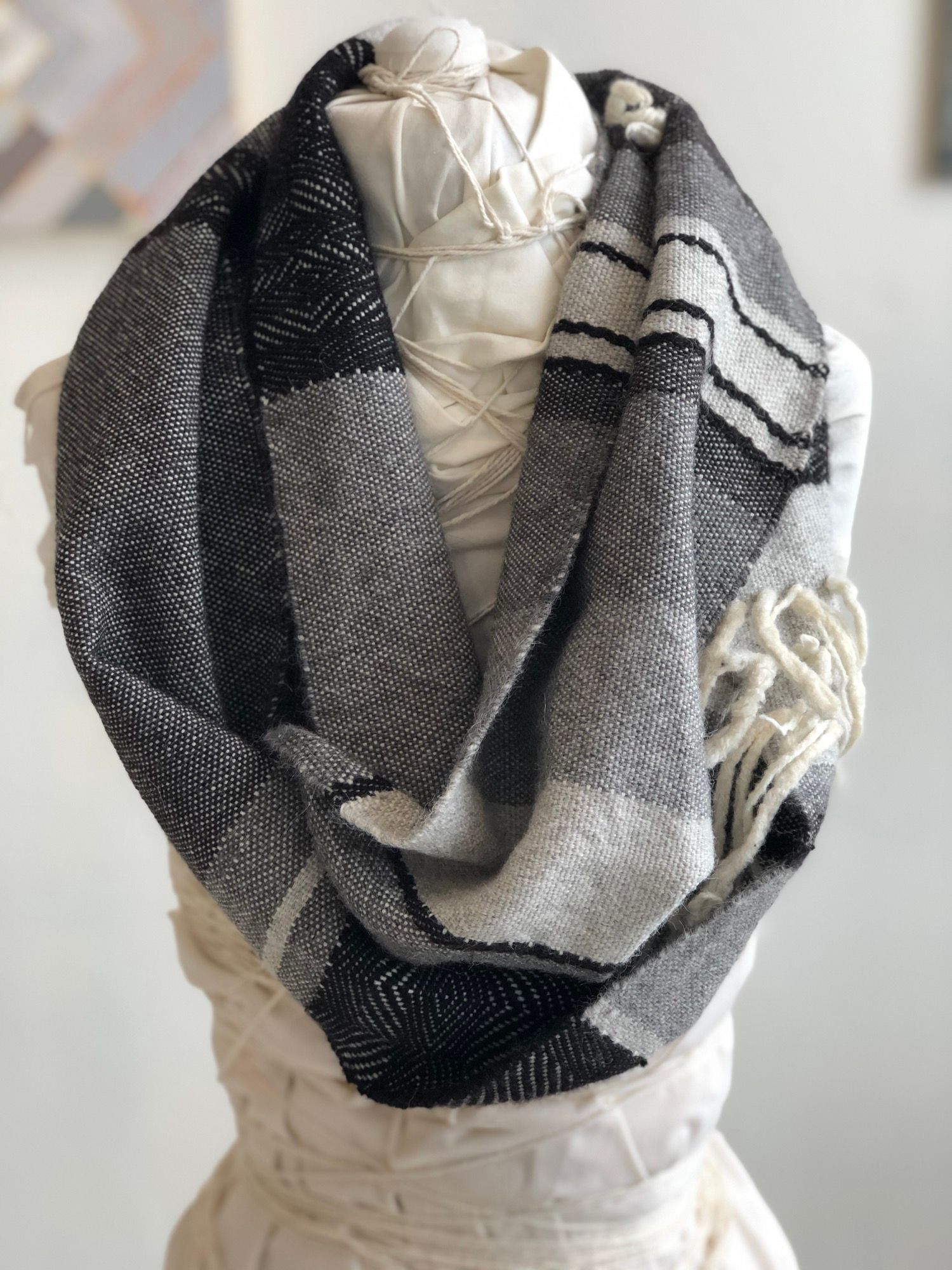 grey, black and white handwoven cowl scarf with fringe on a white mannequin in a white walled gallery
