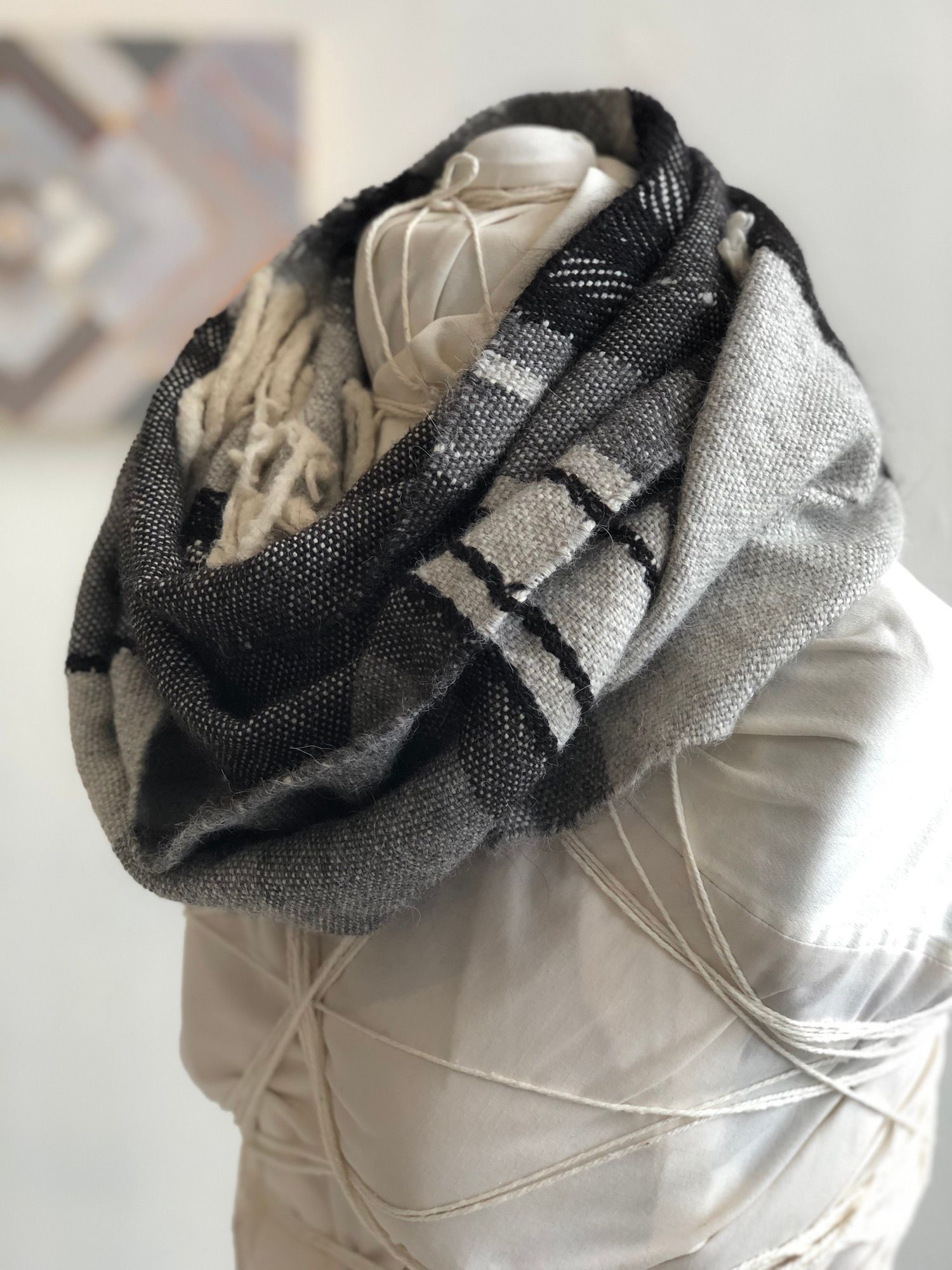grey, black and white handwoven cowl scarf with fringe on a white mannequin in a white walled gallery