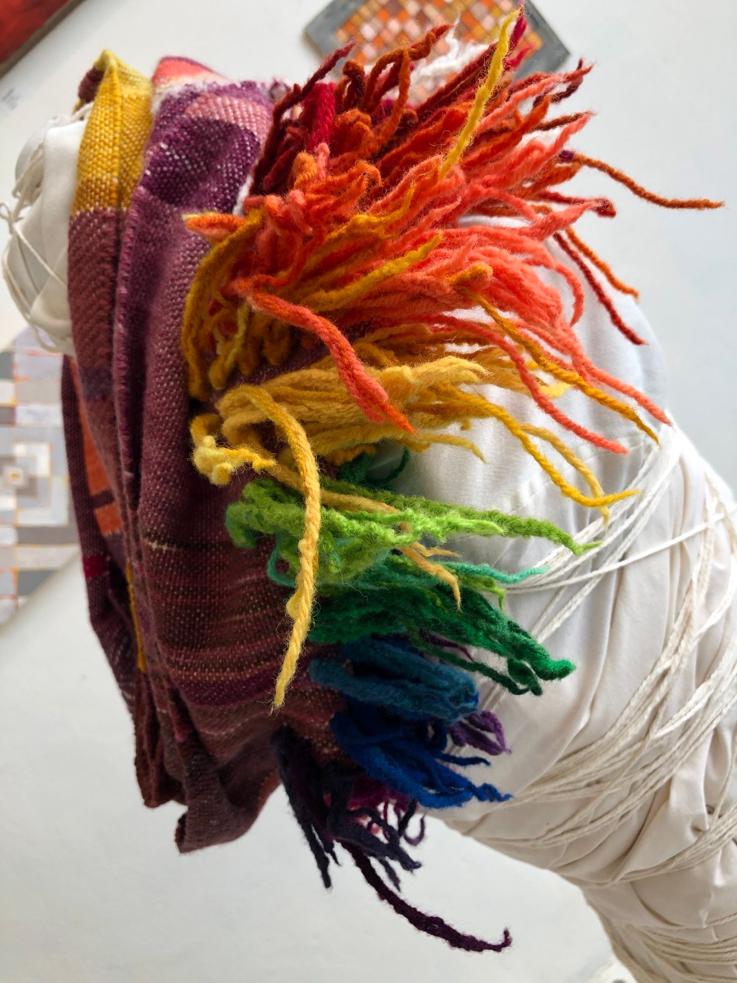 purple, yellow, orange and rainbow handwoven cowl scarf with fringe on a white mannequin in a white walled gallery