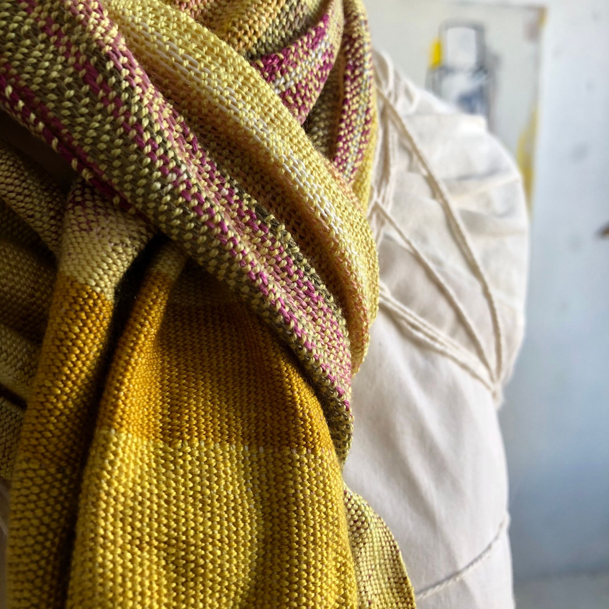 naturally colored scarf on a white mannequin in a gallery with paintings in the background