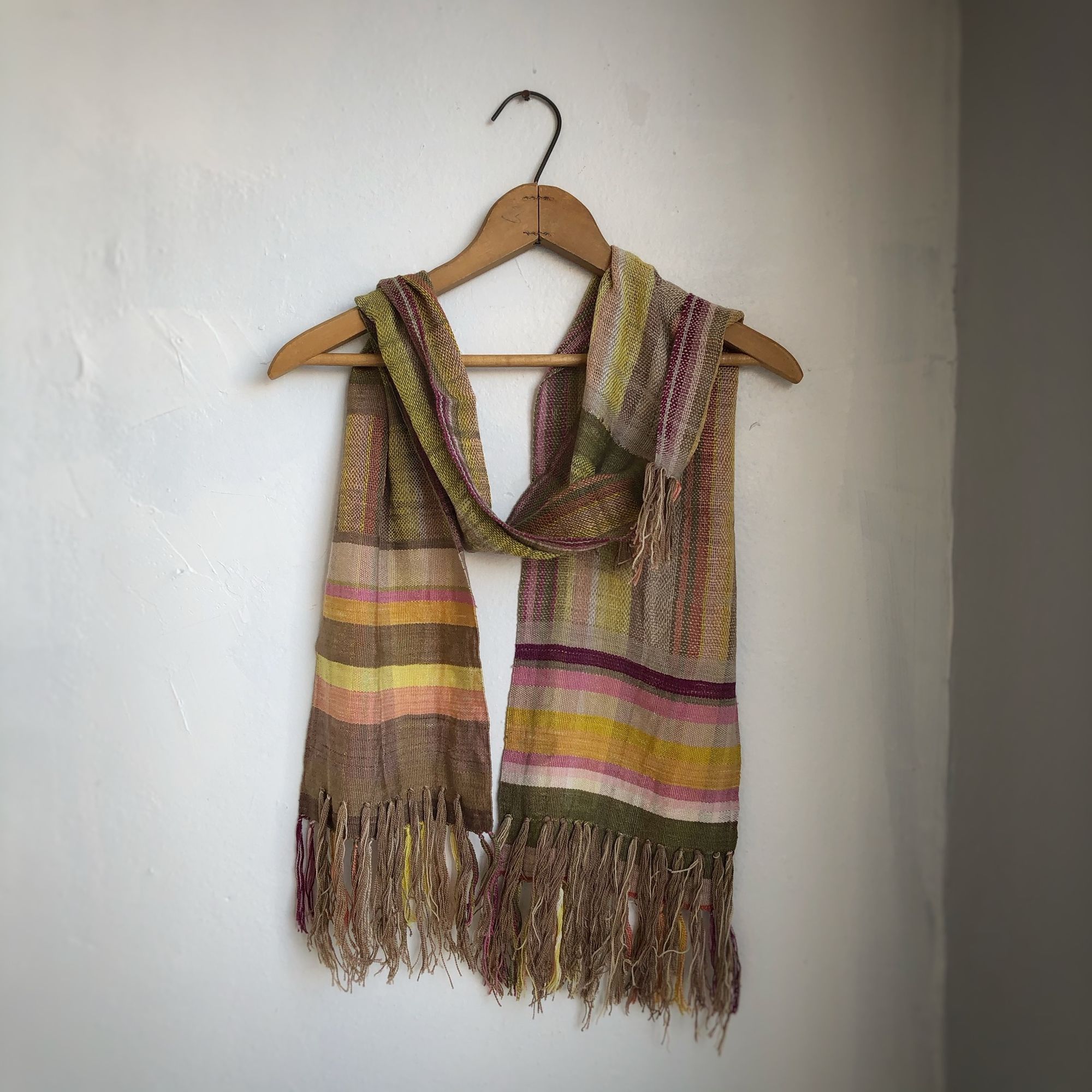 Naturally dyed earth-tone scarf hanging on a hanger on a white wall