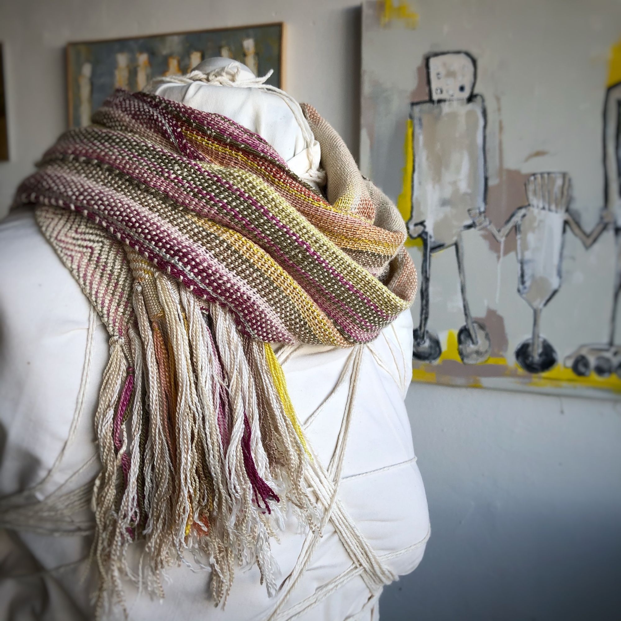 naturally colored scarf on a white mannequin in a gallery with paintings in the background