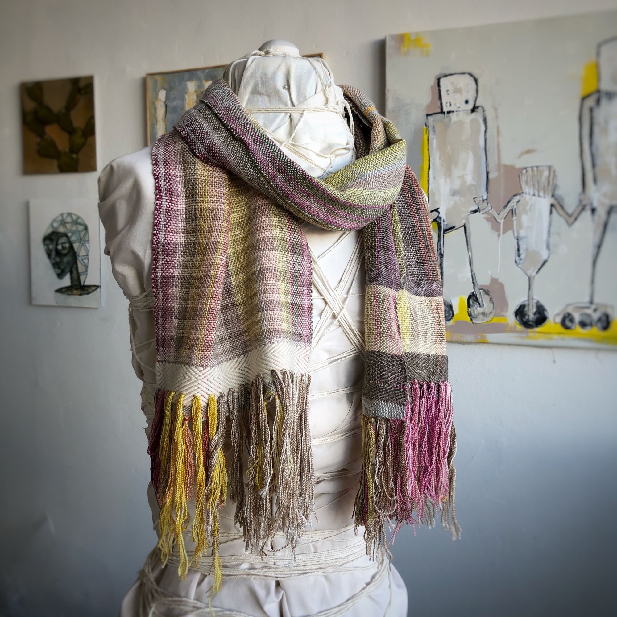 naturally colored scarf on a white mannequin in a gallery with paintings in the background