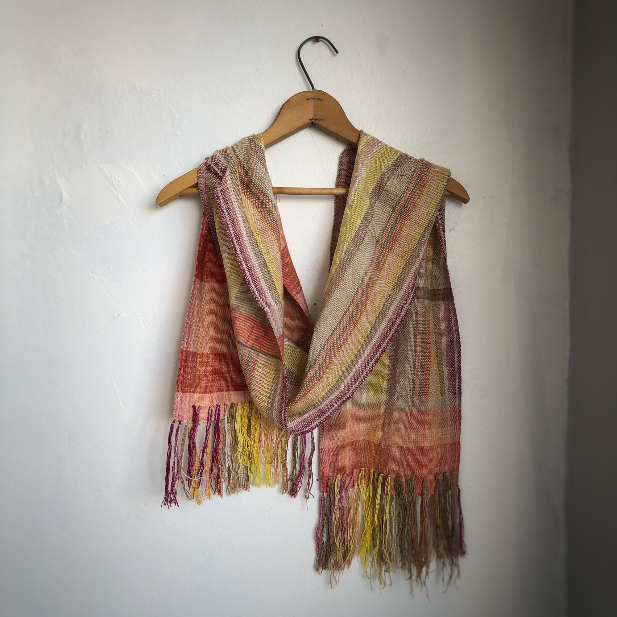 Naturally dyed earth-tone scarf hanging on a hanger on a white wall